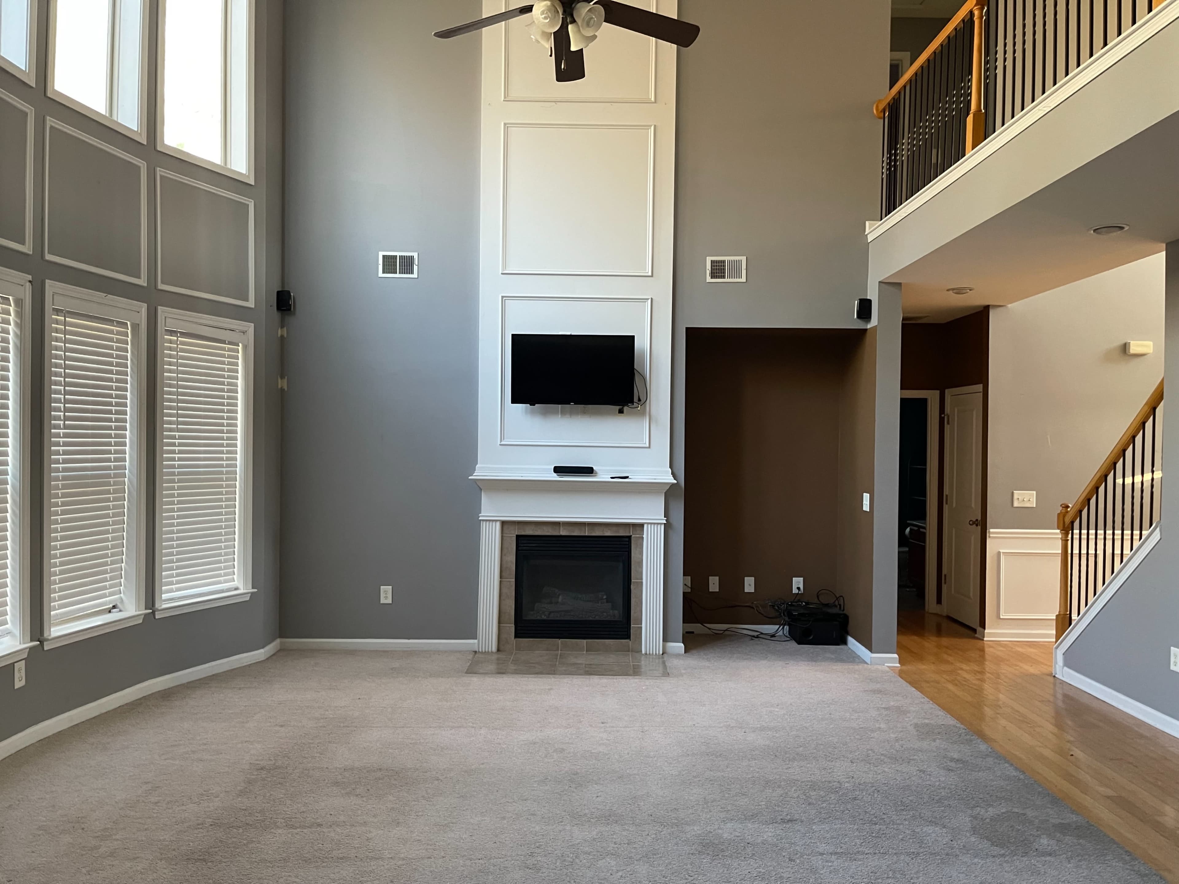 The scene depicts a spacious living room with high ceilings, large windows, a fireplace, and a wall-mounted television.