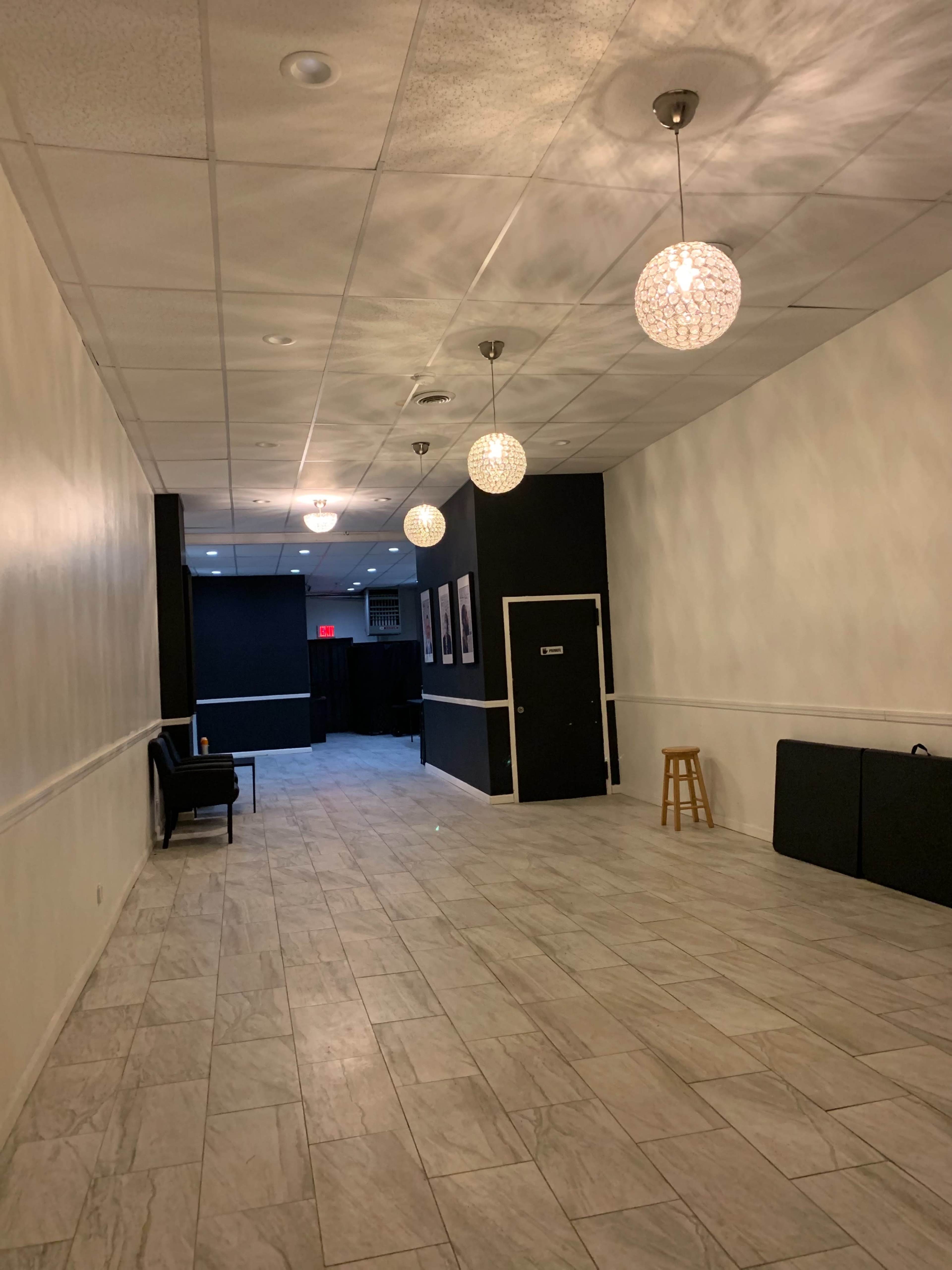 A hallway with tiled flooring, white walls, and decorative light fixtures hanging from the ceiling leads to a door at the far end.