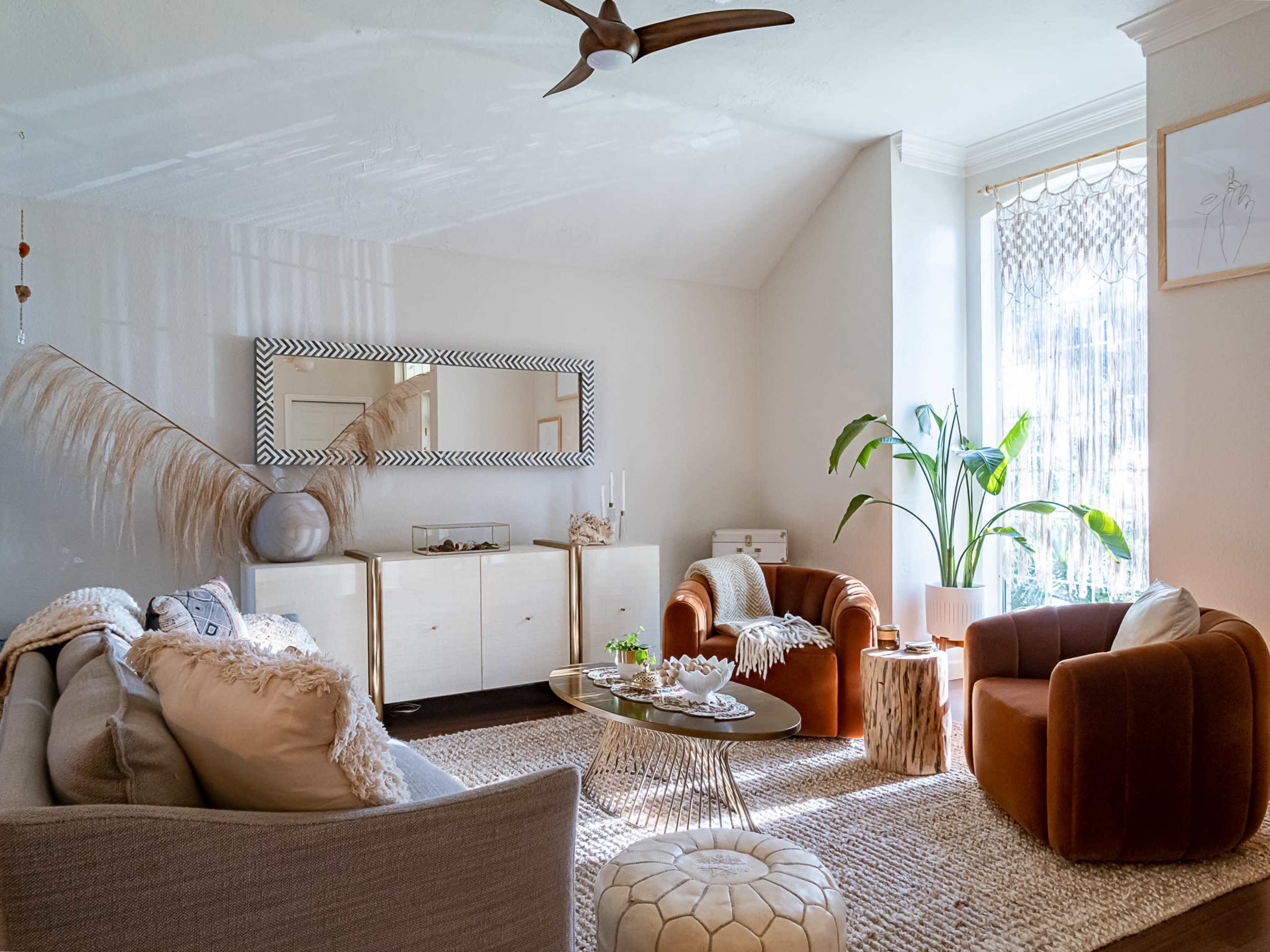 The living room features two armchairs, a beige sofa, a decorative mirror, a light rug, and a potted plant near a window.