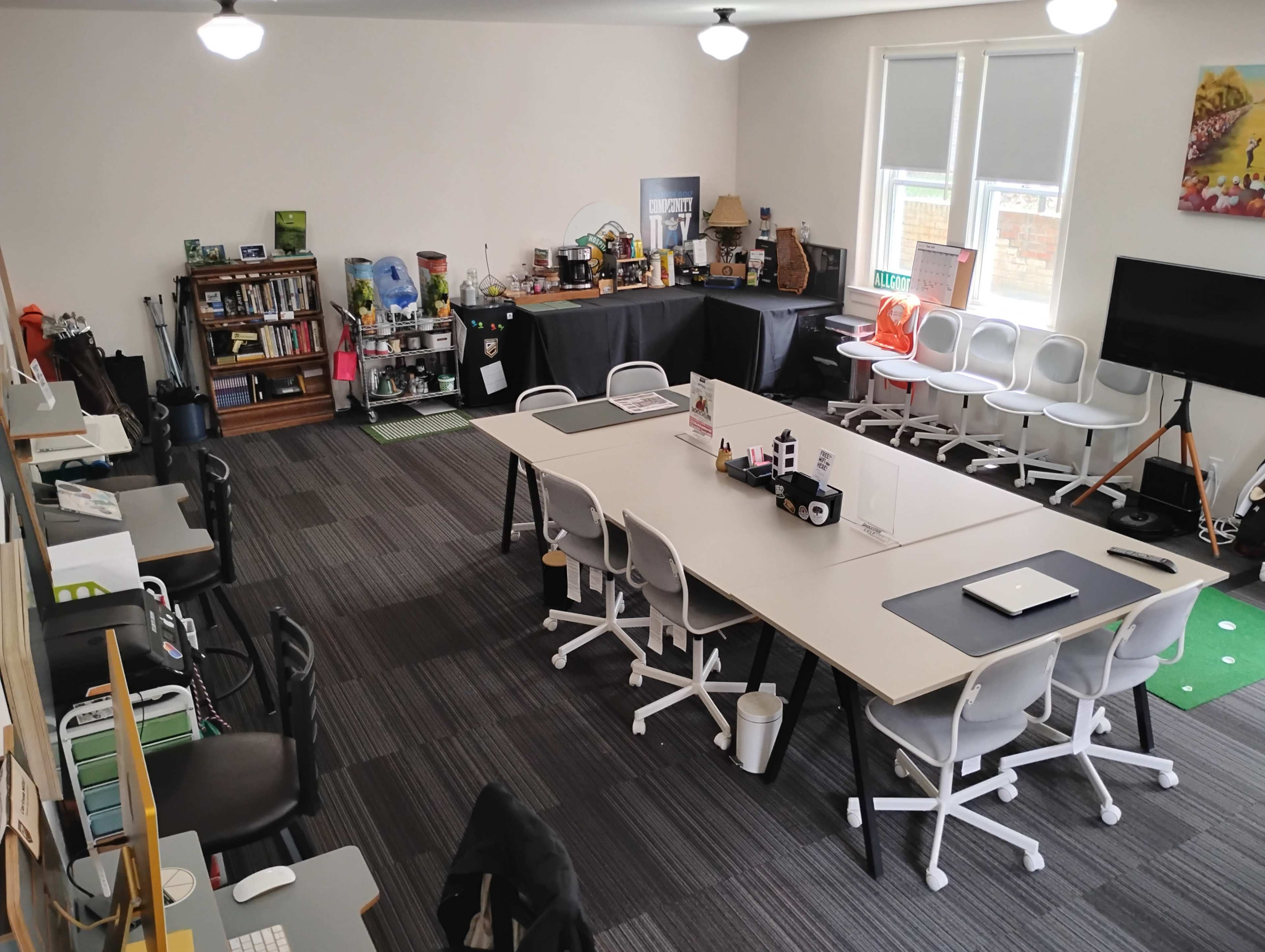 The image shows a spacious office with multiple workstations, a central table, and various decorative items on display.