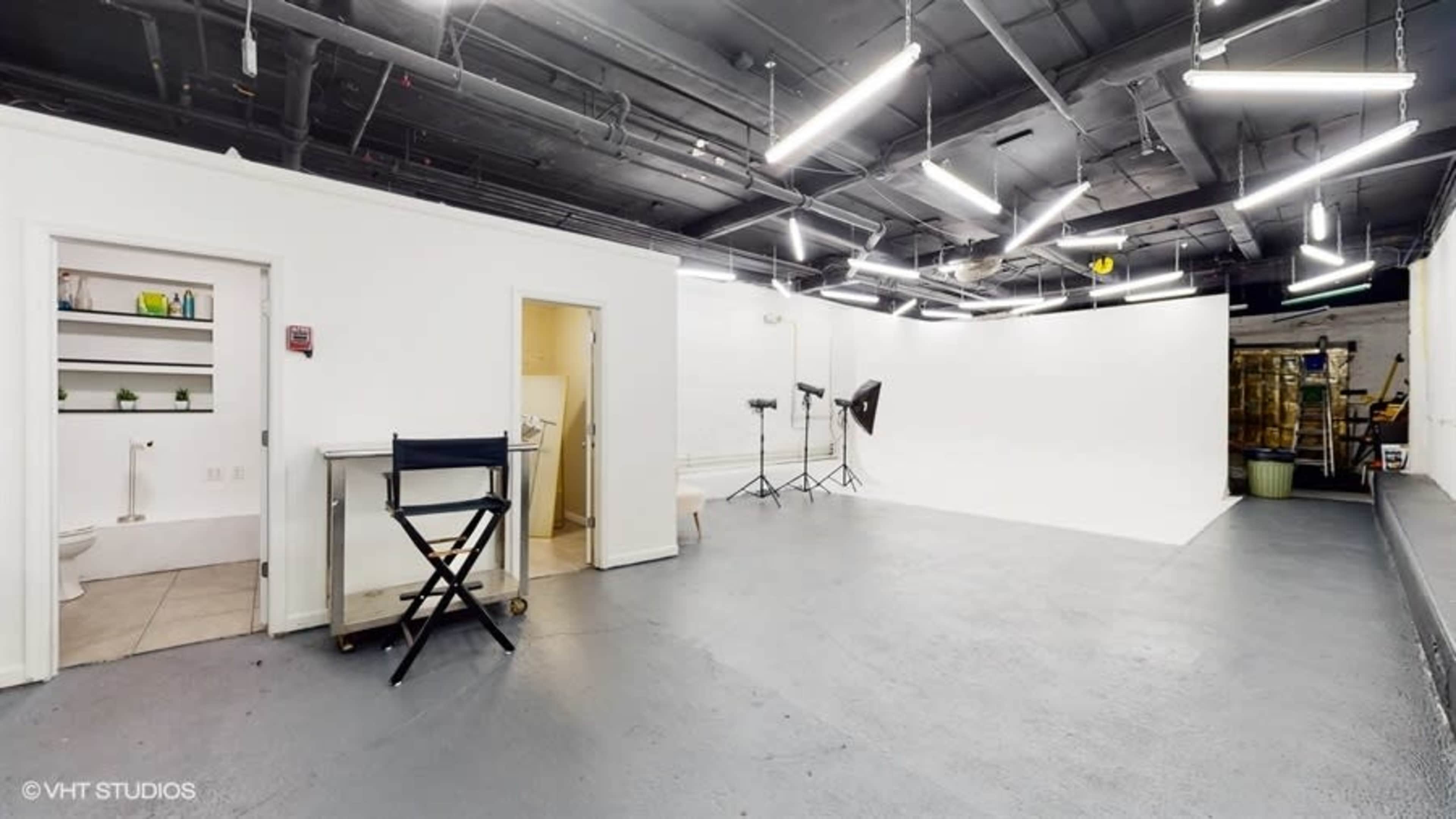 A photography studio with a white backdrop, two lights on stands, and a restroom area in the corner.