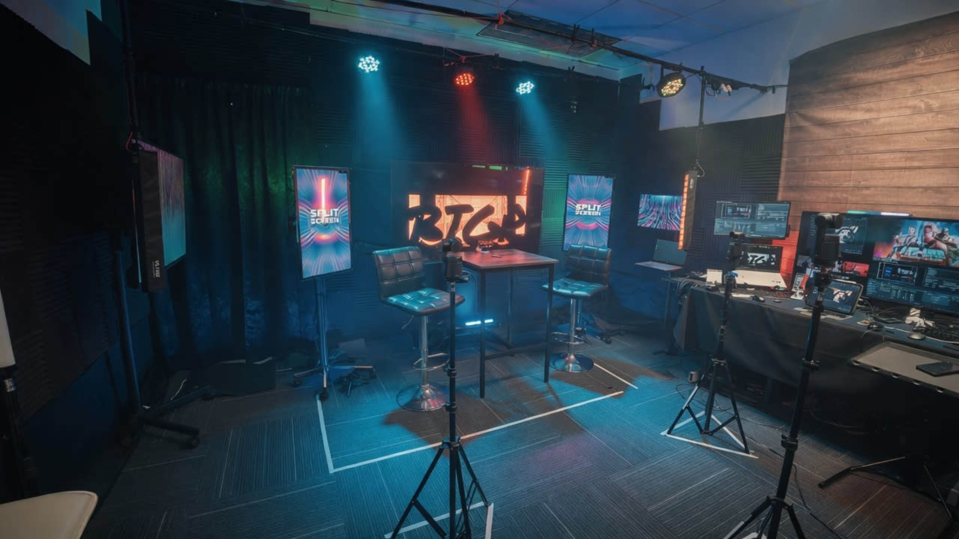 The image shows a well-equipped studio setup with two stools, multiple monitors displaying graphics, and various lighting fixtures.