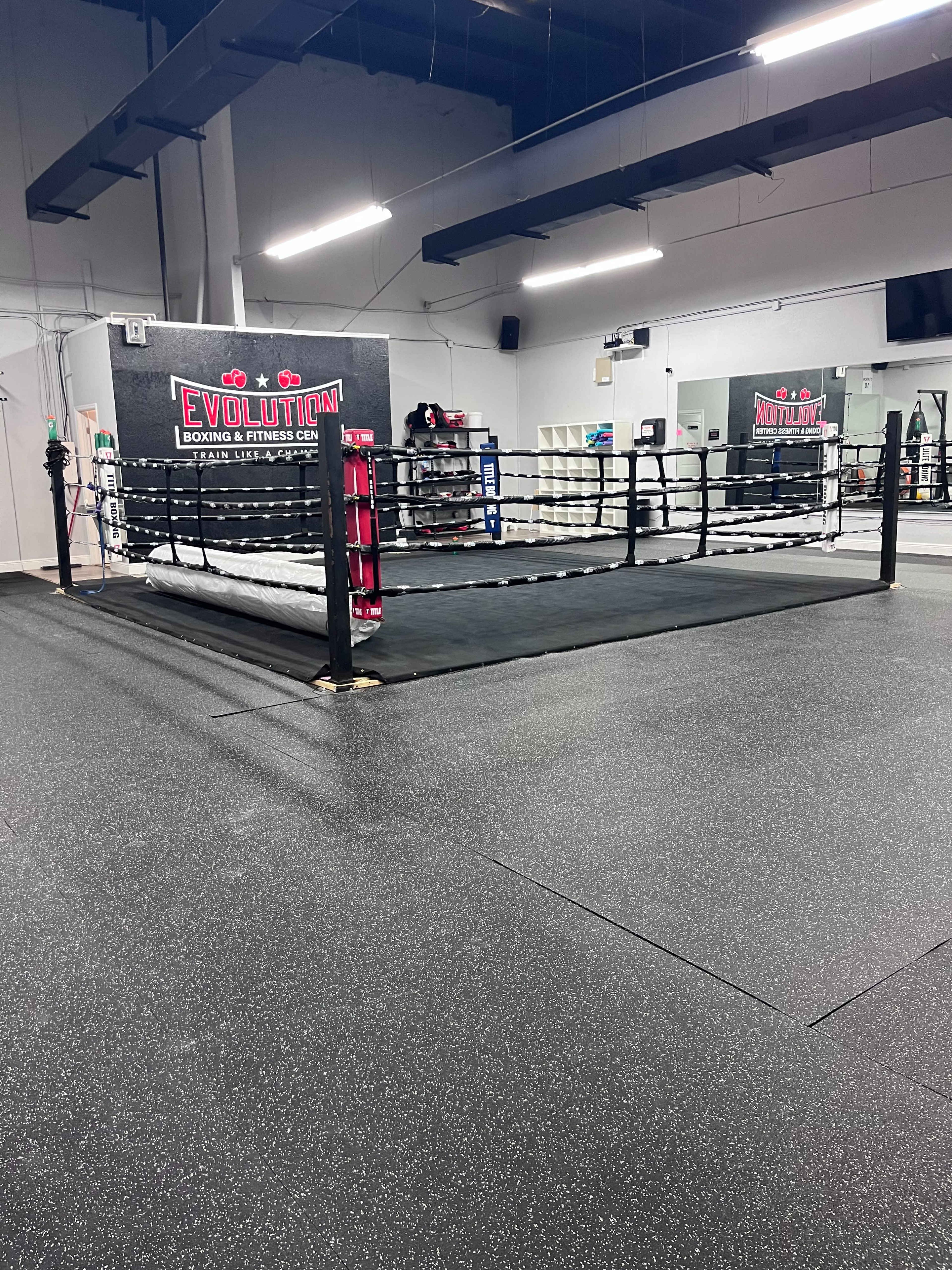 A boxing ring in a gym with a rubberized floor and a wall featuring the word "EVOLUTION."