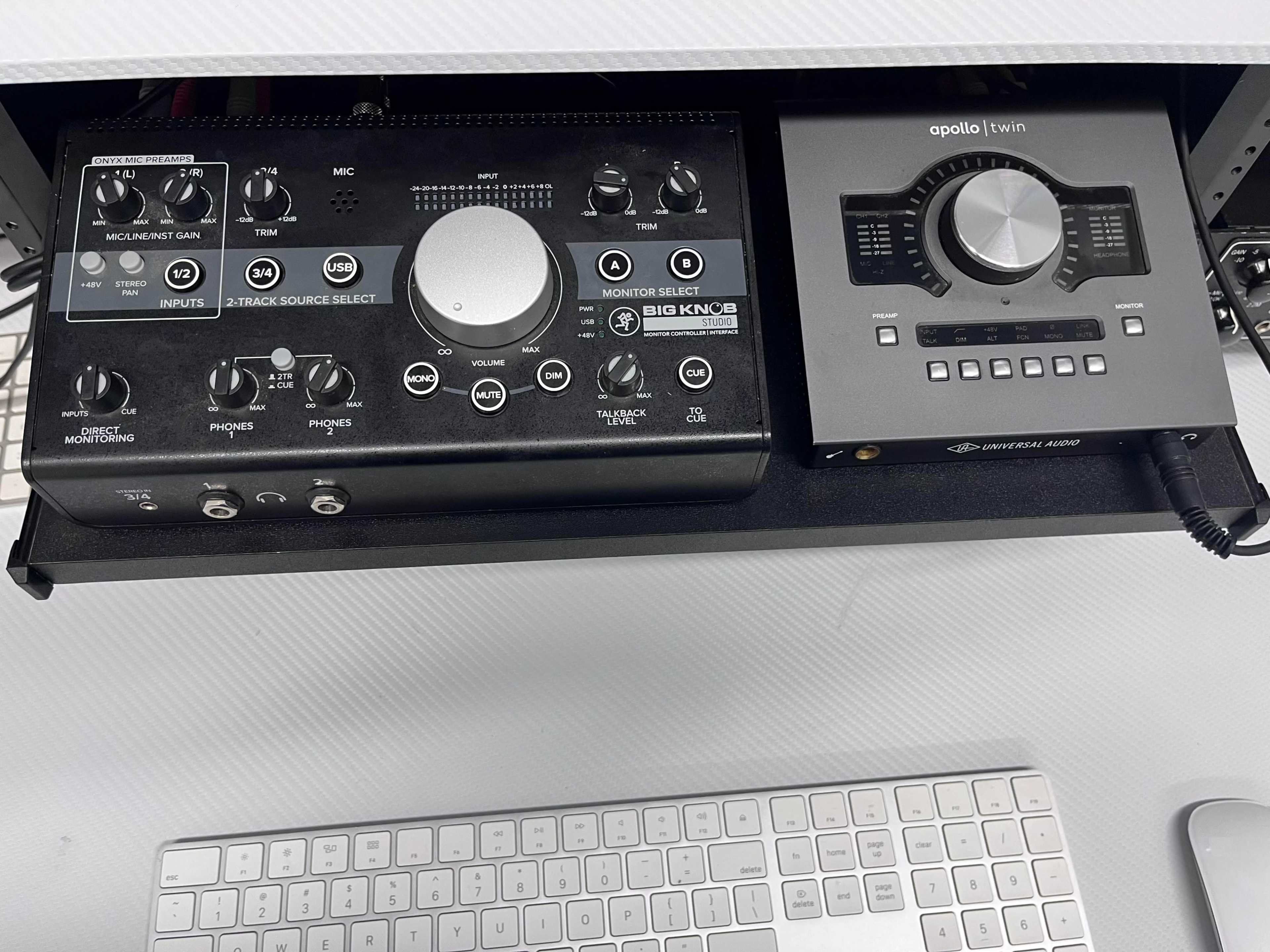 A close-up of a studio equipment rack featuring a audio interface and a monitoring controller, along with a keyboard in the foreground.