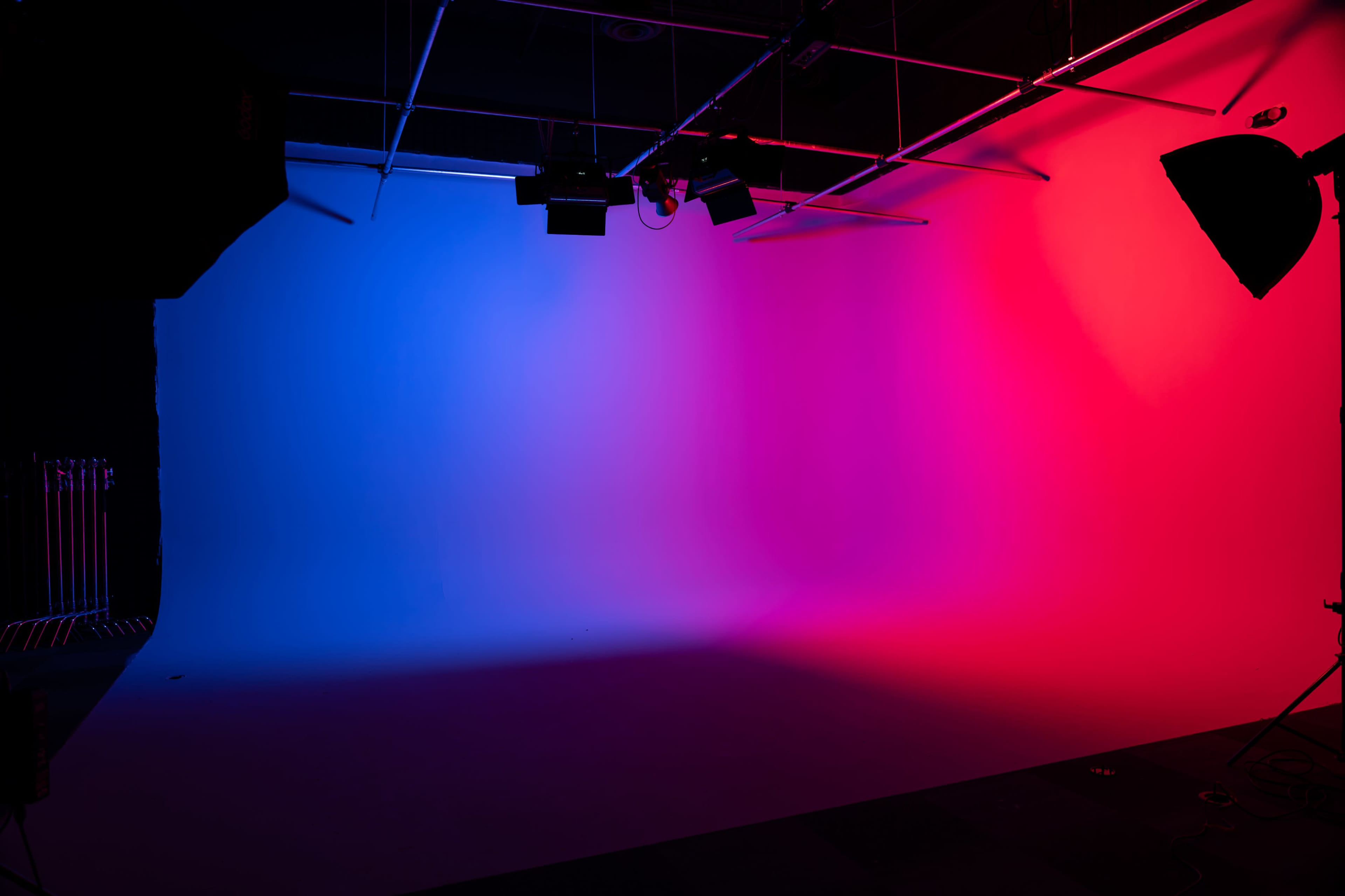 The image shows a photography studio with a gradient background transitioning from blue to pink, illuminated by lights.