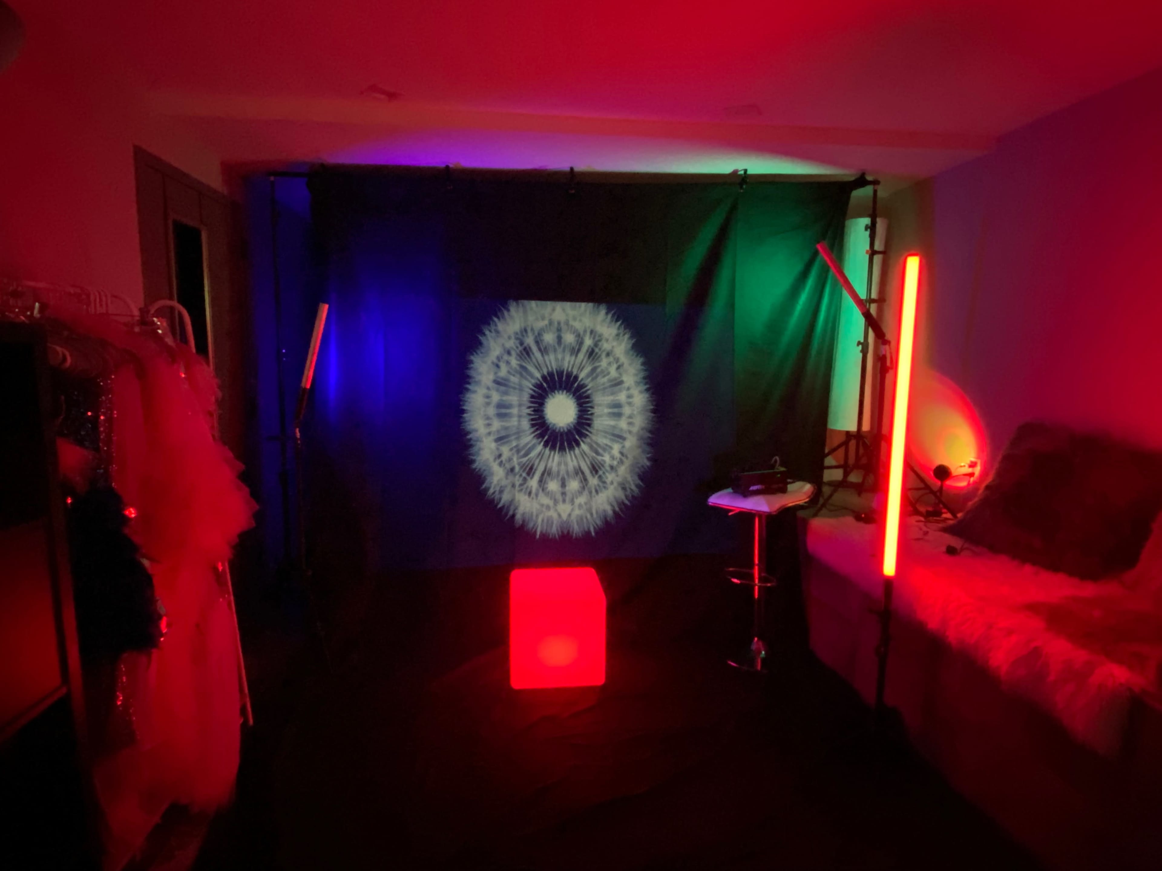 A dimly lit room with a black backdrop displaying a circular light pattern, flanked by colored lighting and featuring a red illuminated cube in the center.