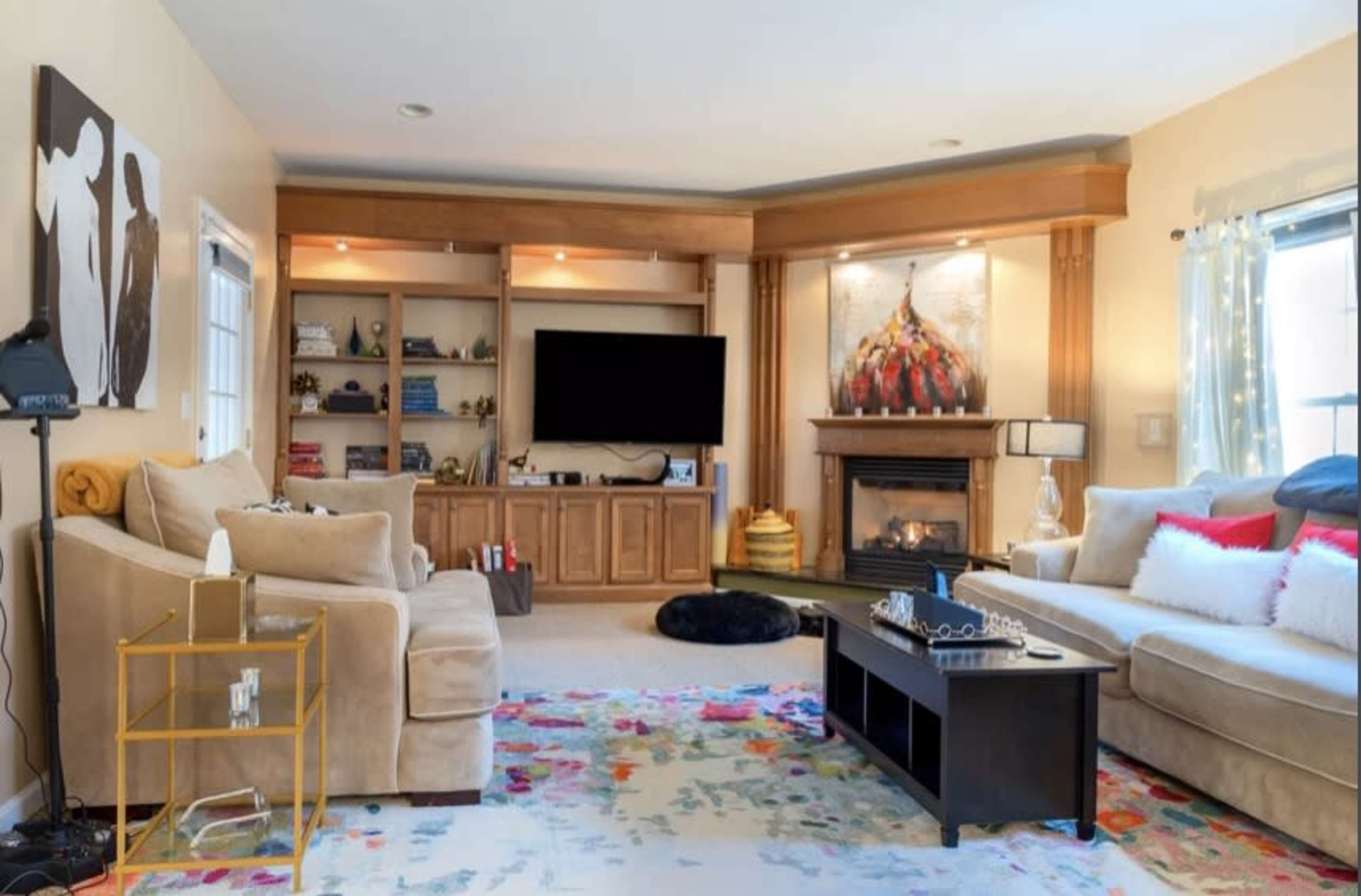 A cozy living room features a fireplace, a large television, and a mix of comfortable seating arranged around a colorful area rug.