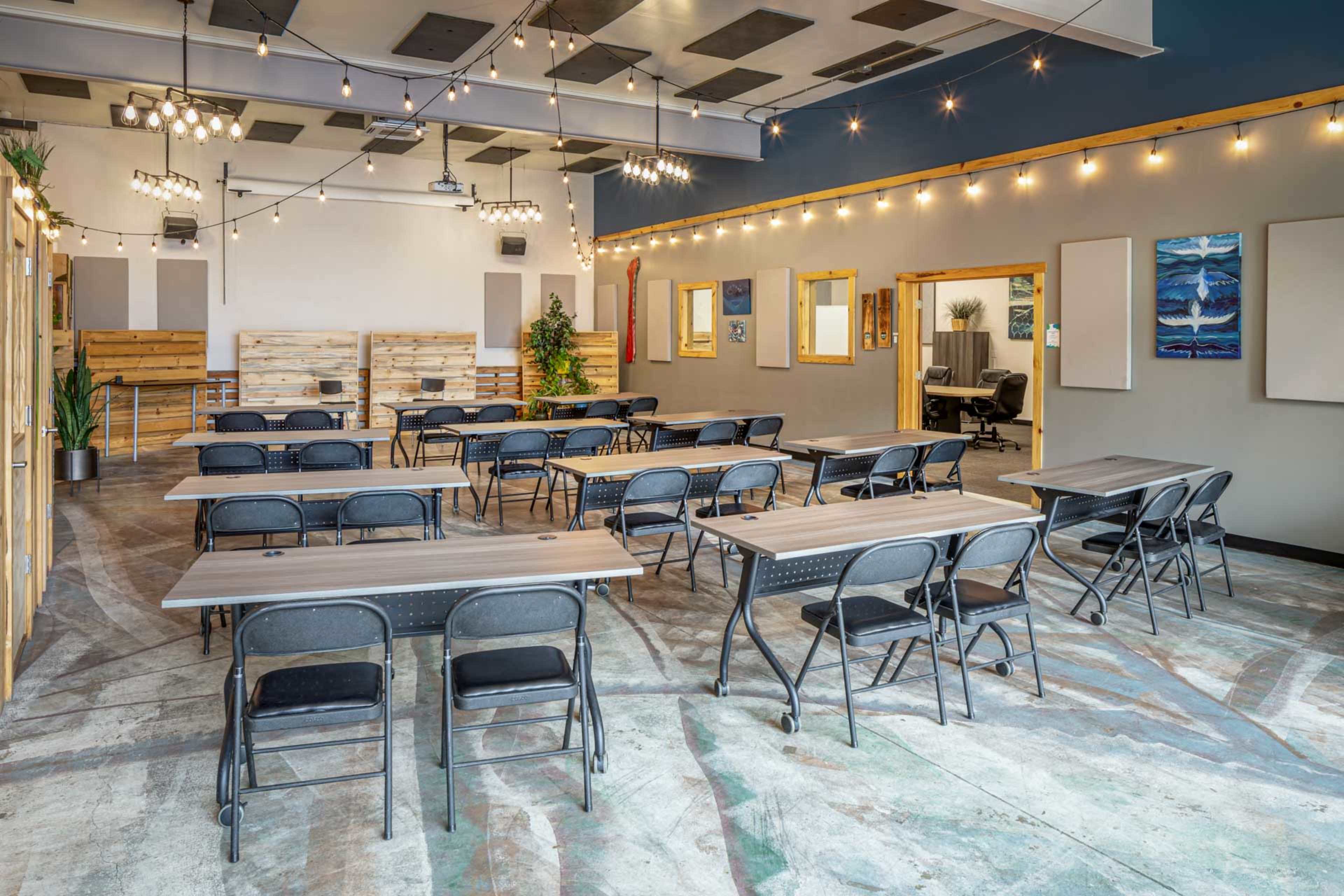 A spacious classroom with tables and chairs arranged for a meeting, featuring string lights and wall art.