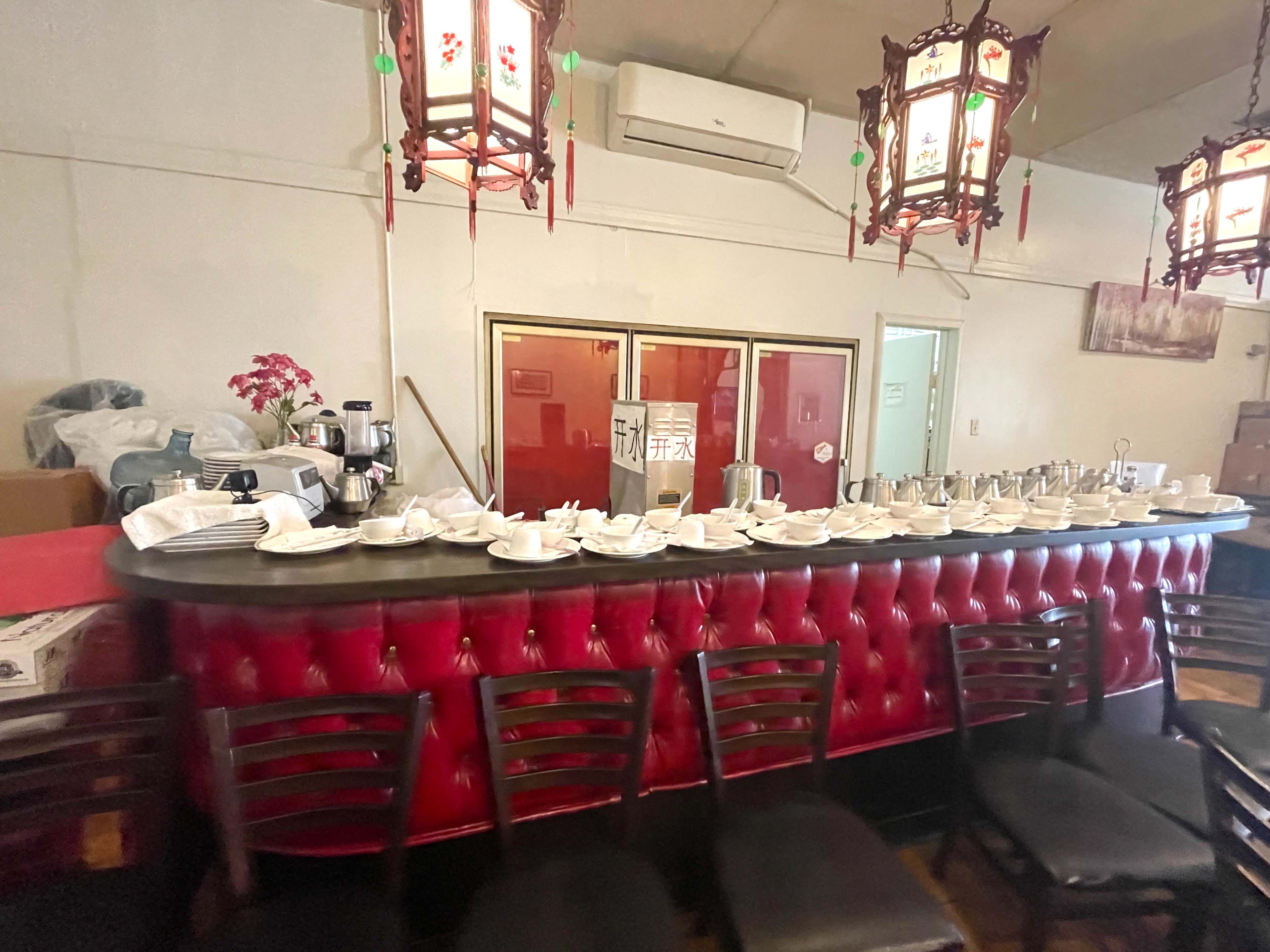 The image shows a red velvet bar with various teapots and dishes arranged on top, set against a backdrop of wall décor and hanging lanterns.