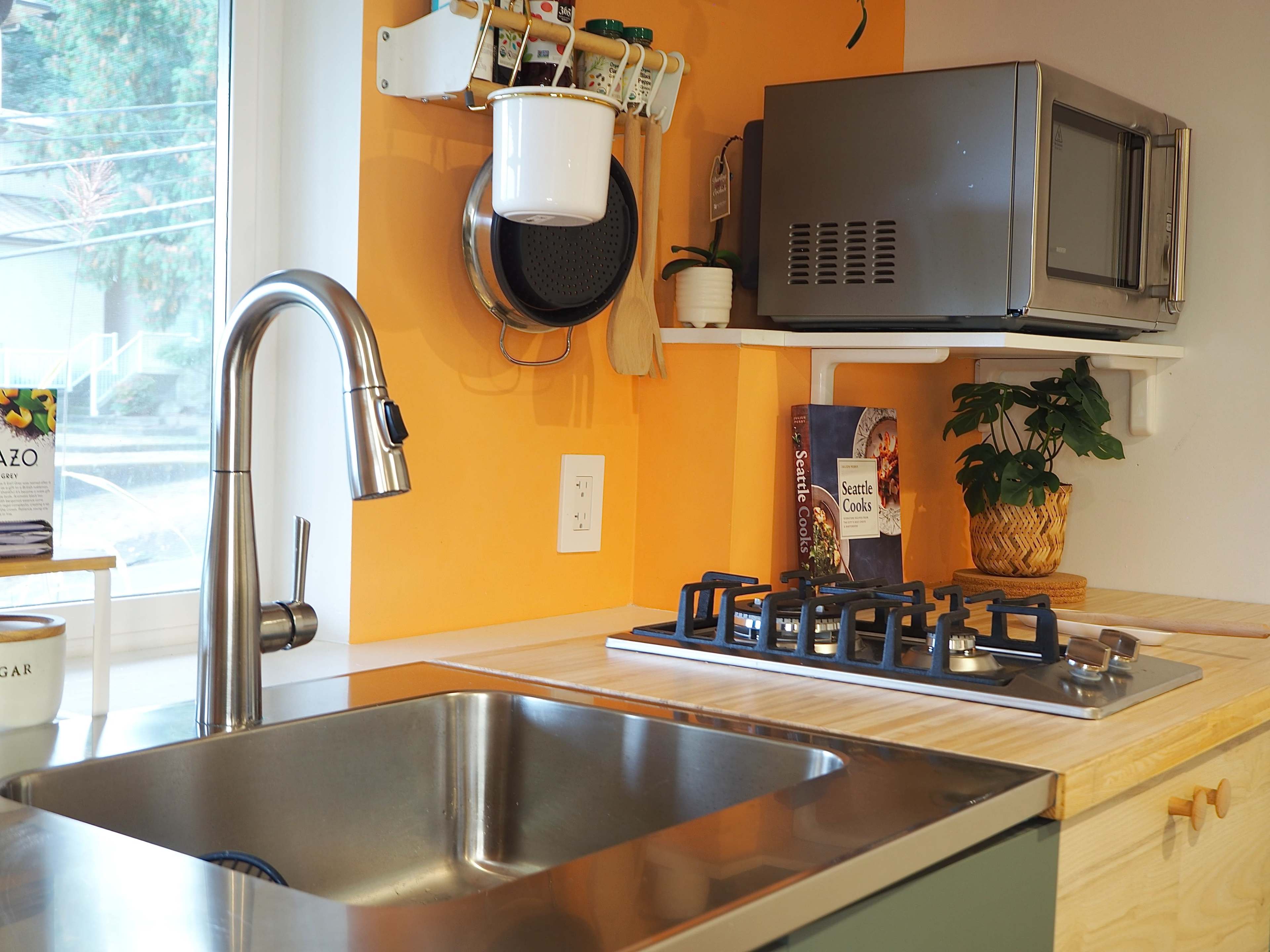 A kitchen with a stainless steel sink, a gas stove, a microwave, and bright orange walls.