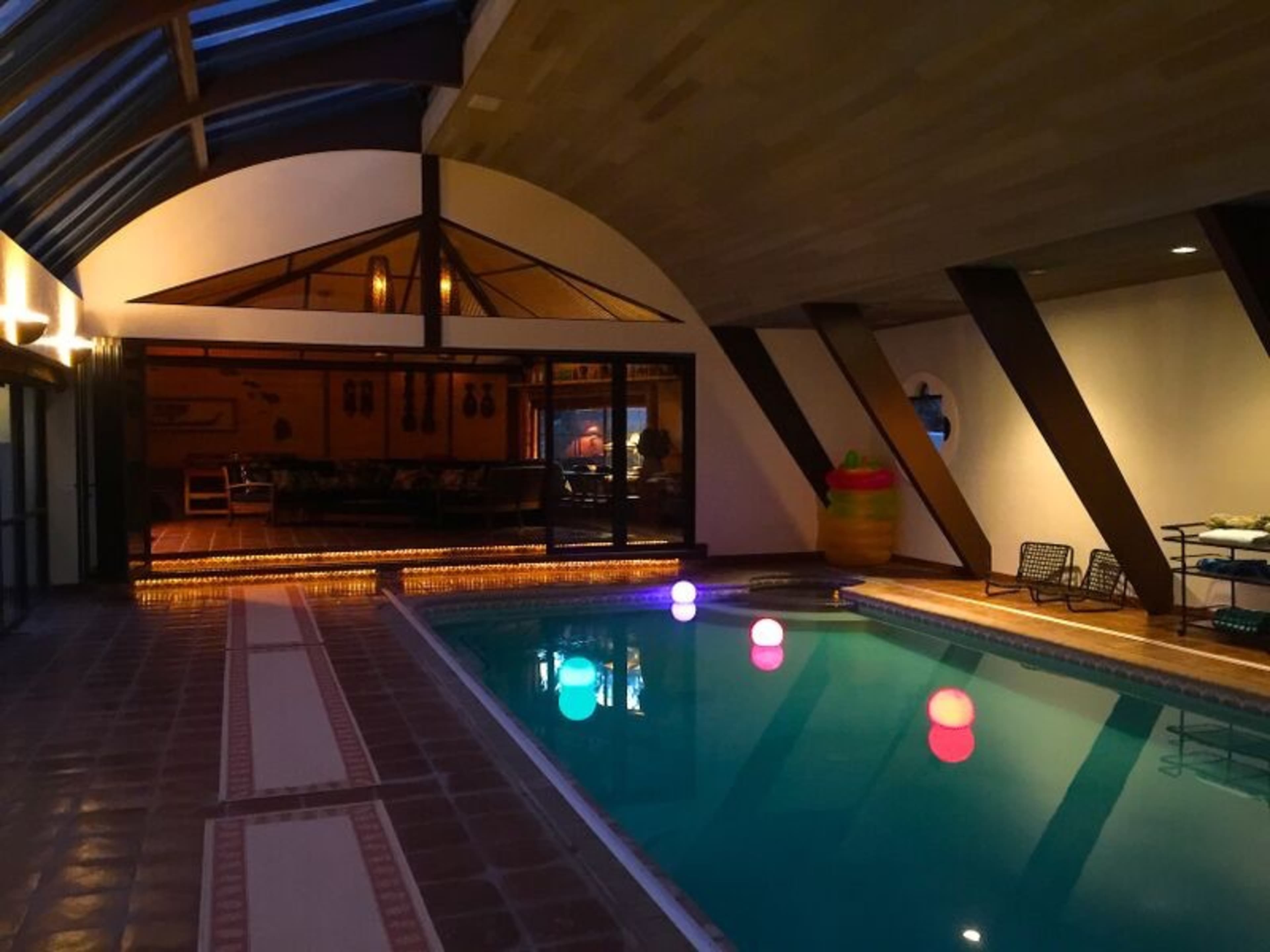An indoor pool area features colorful floating lights and a large window overlooking a dining space.