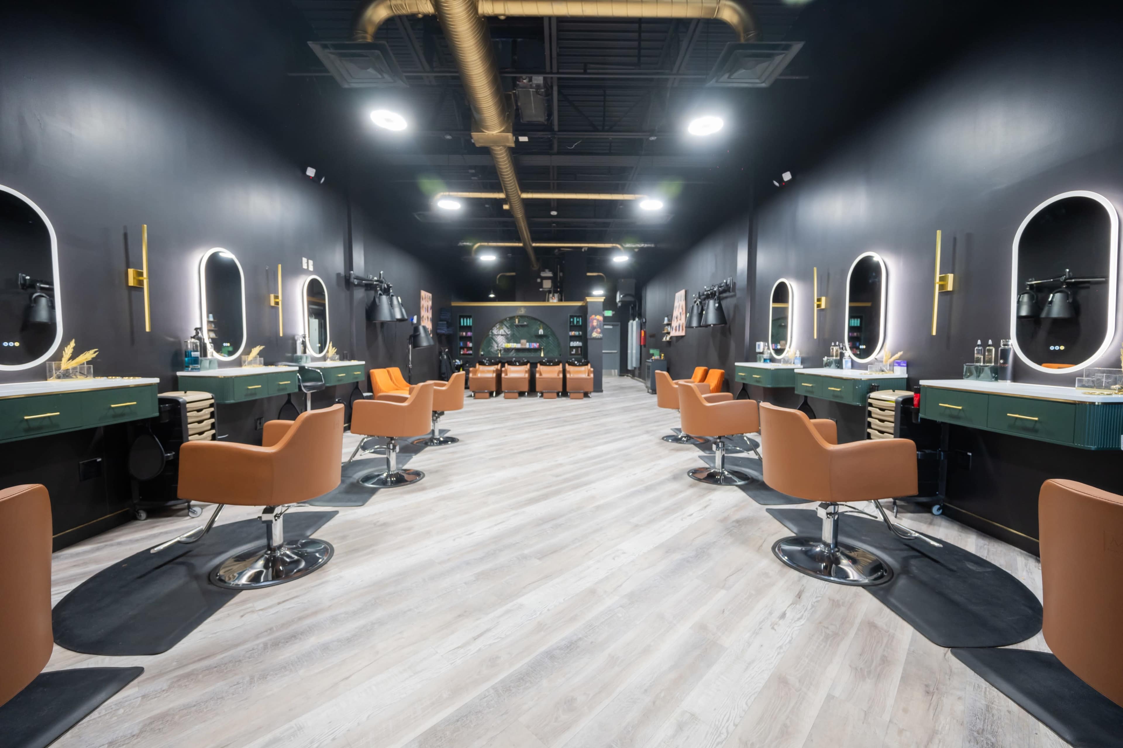 The image shows a modern hair salon with several styling stations equipped with orange chairs, circular mirrors, and a sleek black and green color scheme.