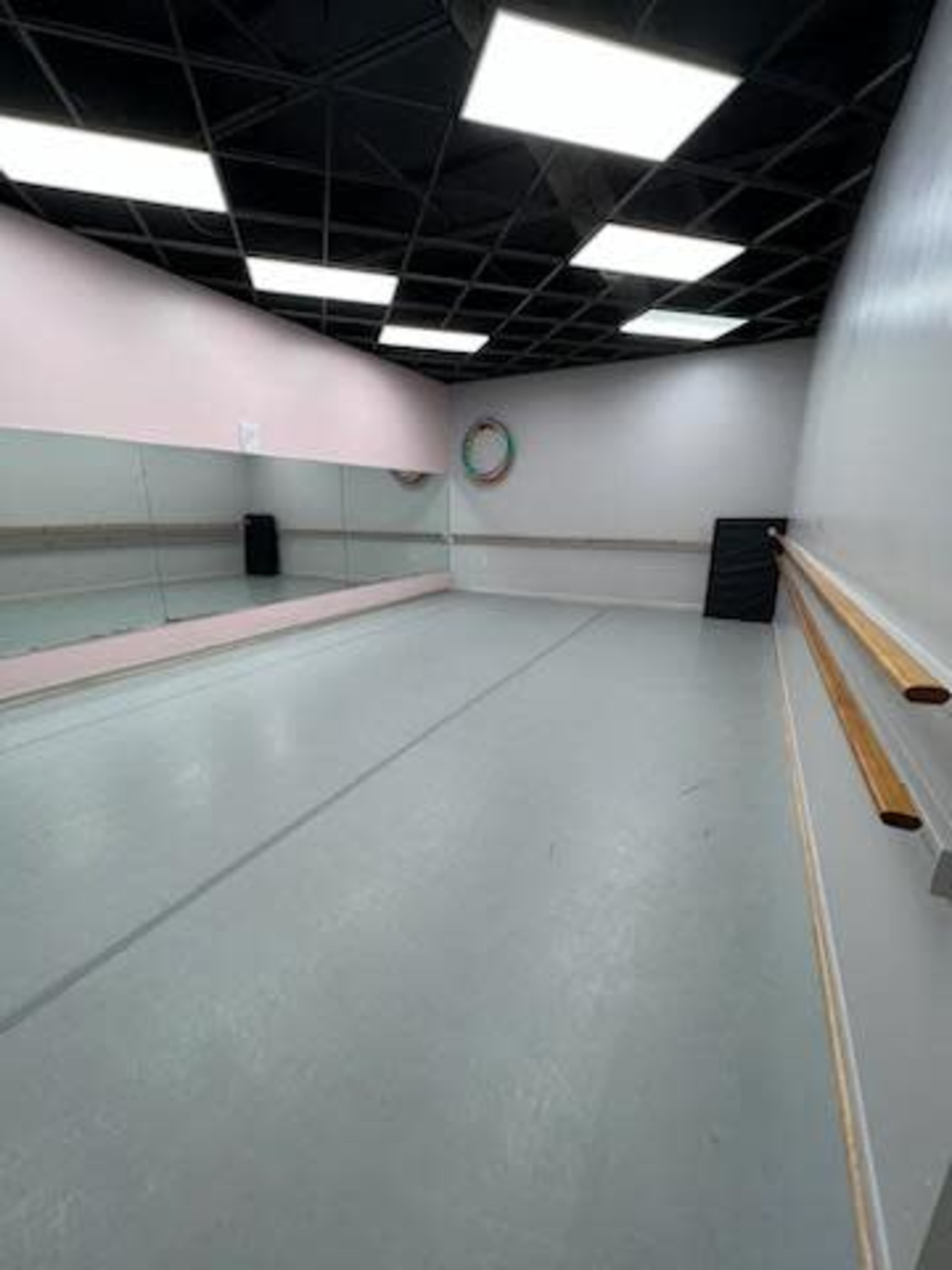 The image shows an empty dance studio with a mirrored wall and ballet barre along one side, illuminated by overhead lights.
