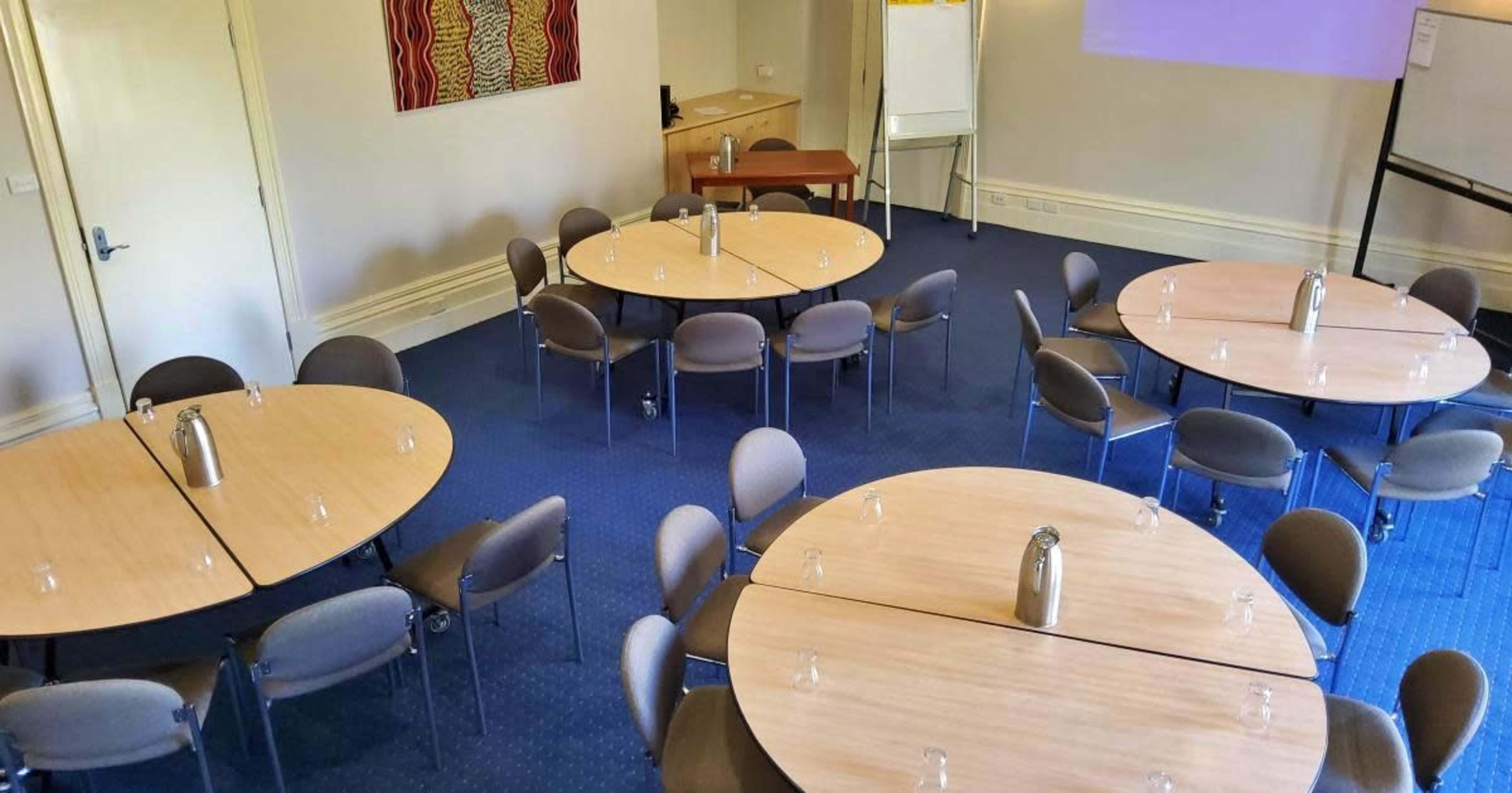 The image shows a conference room with several round tables arranged in a layout, each equipped with a water jug and glassware.