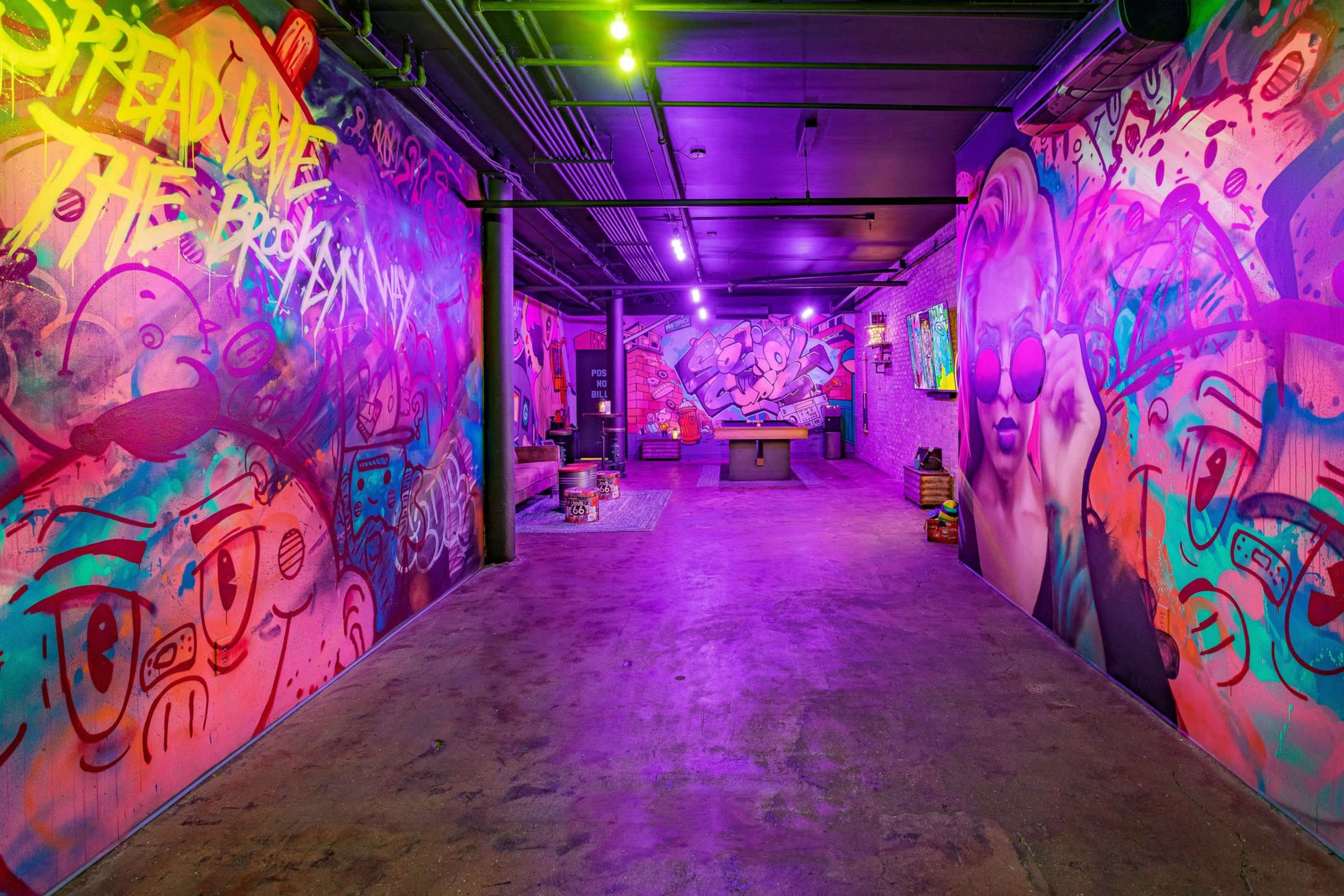 The image shows an artistic underground space with vibrant graffiti on the walls and colorful lighting creating a lively atmosphere.