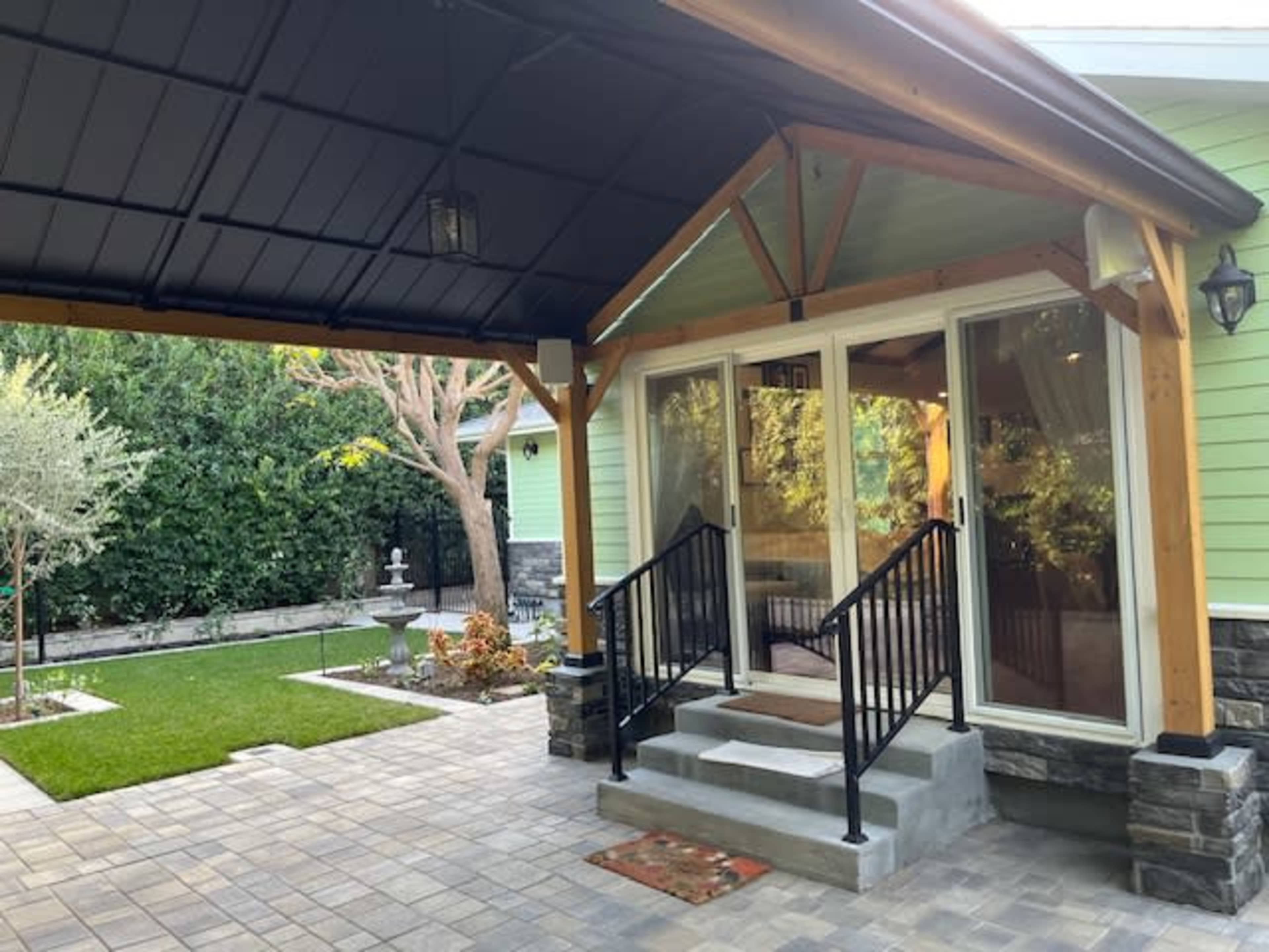 The image shows a small patio area leading to glass doors, surrounded by greenery and stone pathways.