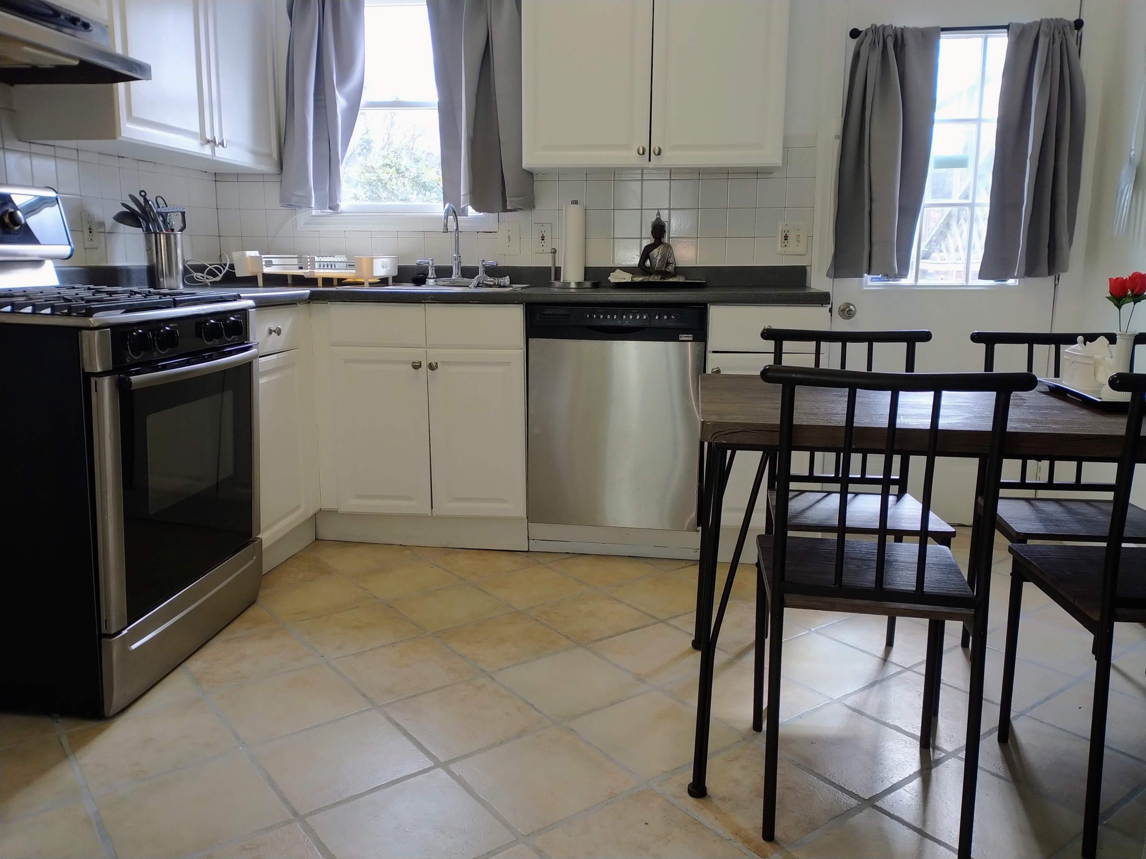 A kitchen with a stainless steel oven and dishwasher, white cabinets, and a small wooden dining table with metal chairs.