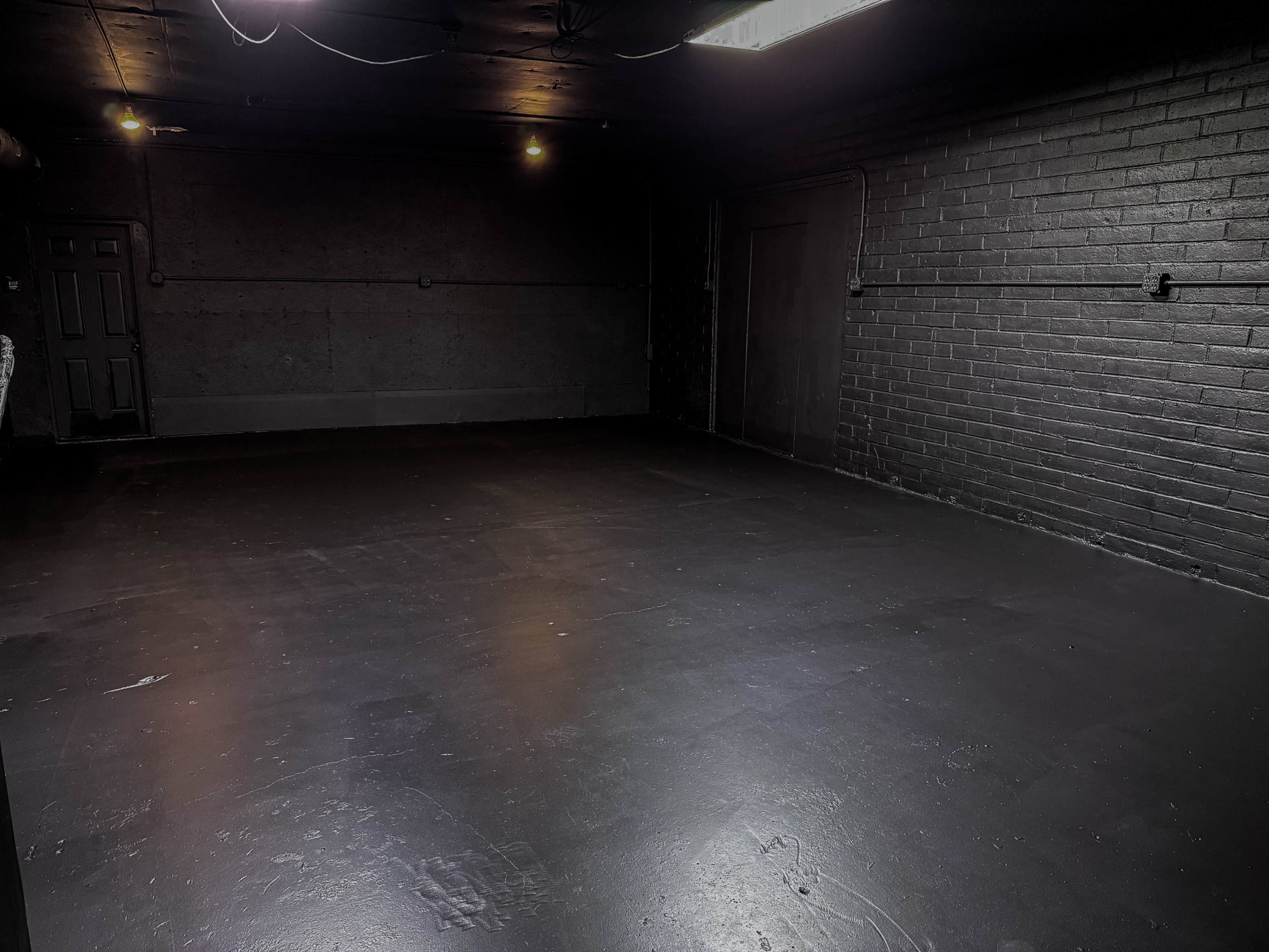 The image shows a dimly lit, empty room with black-painted walls and a floor.