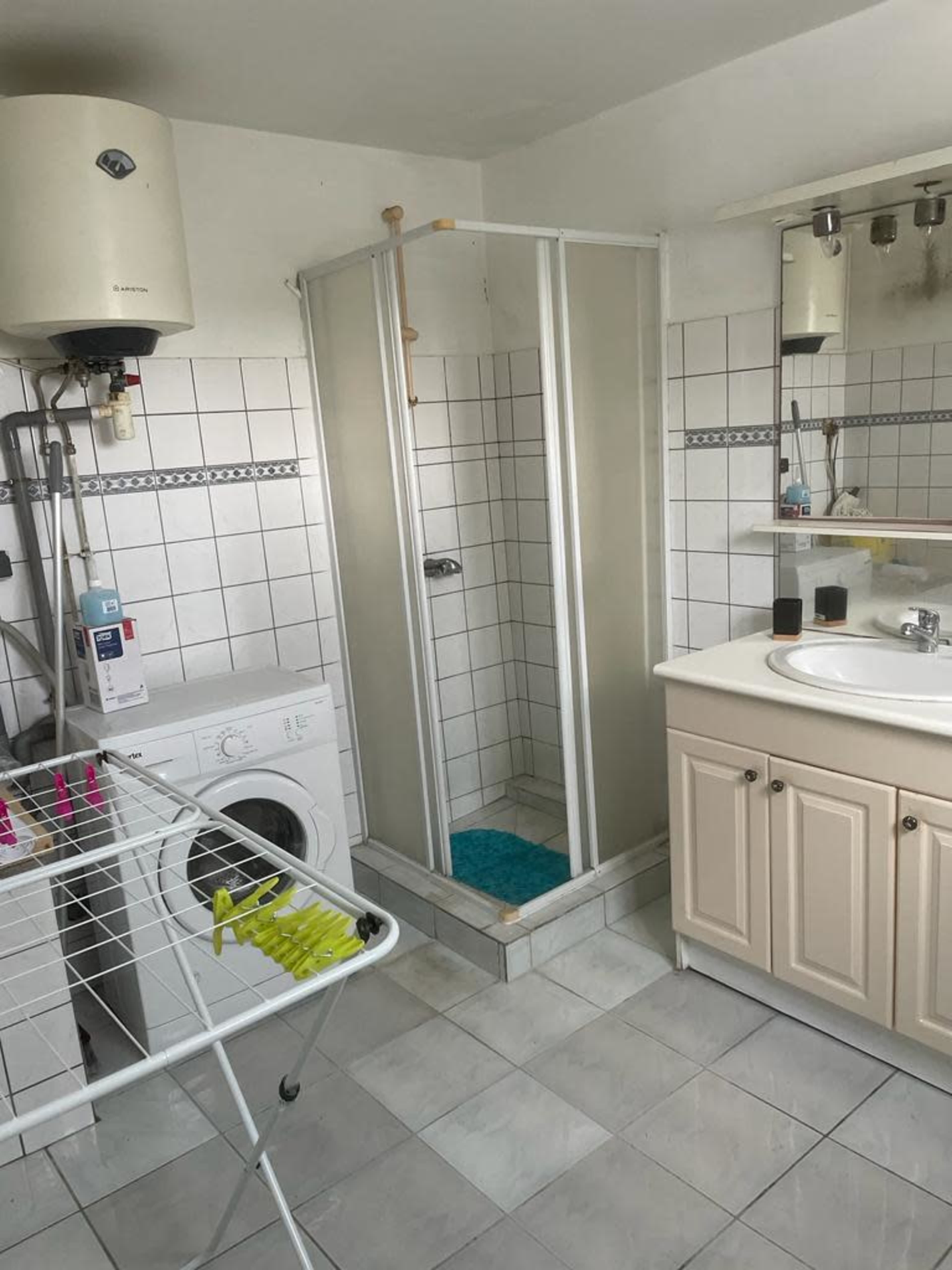 A bathroom with a shower stall, washing machine, vanity with mirror, and a clothes drying rack.