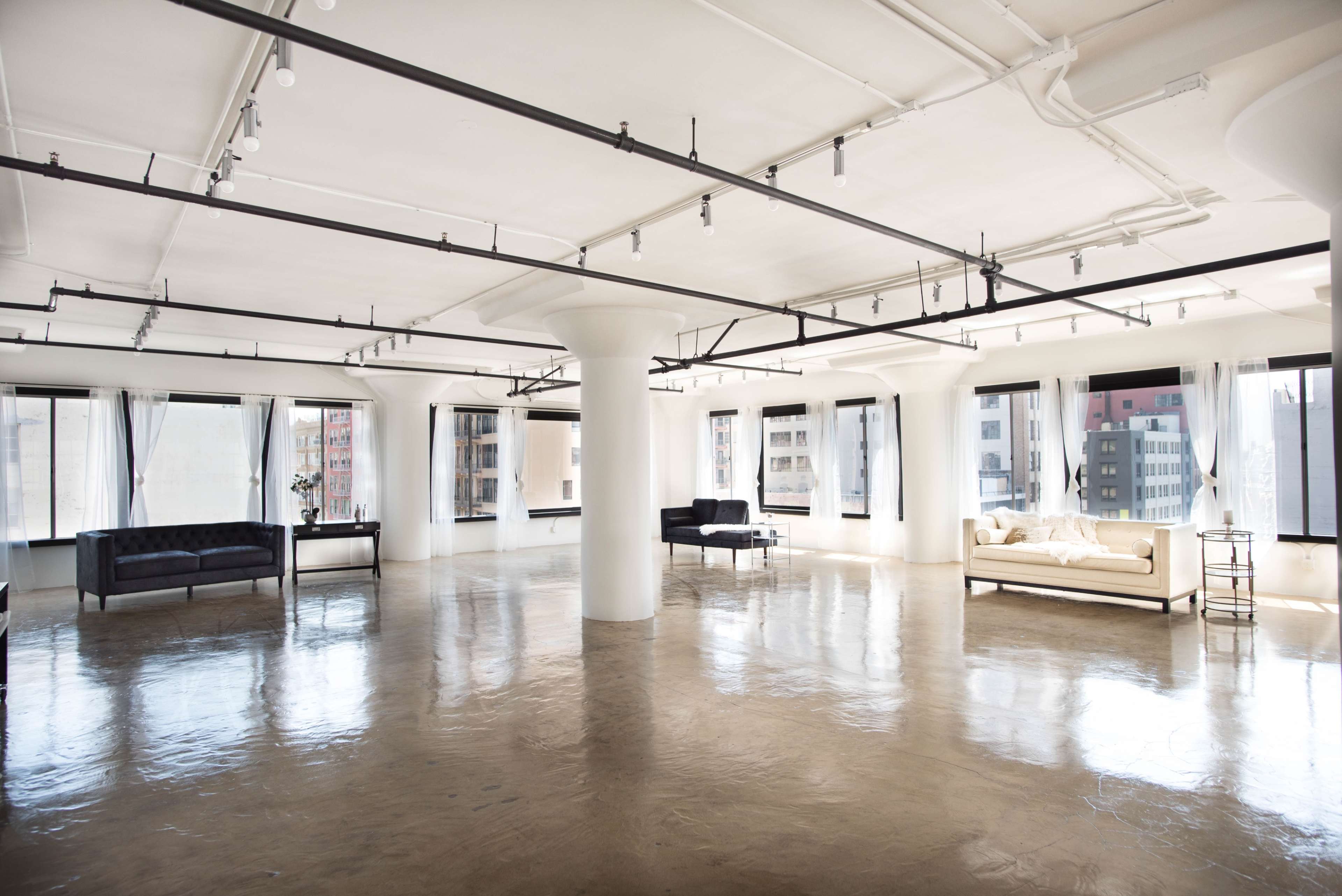 A spacious, empty room with polished concrete floors, large windows, and minimal furniture including two sofas and a coffee table.