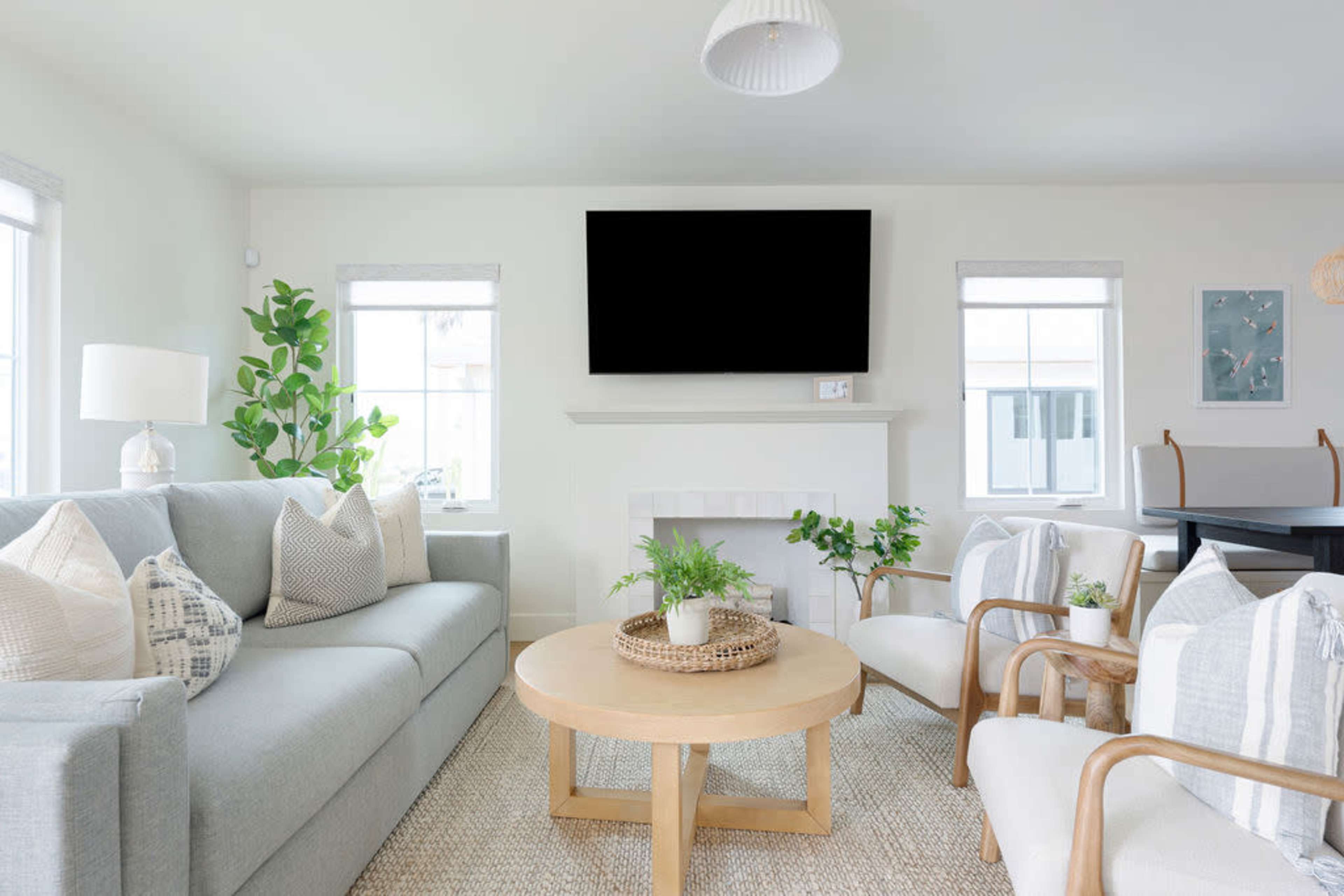 A modern living room with a light gray sofa, two armchairs, a round wooden coffee table, and a large television mounted above a white fireplace.