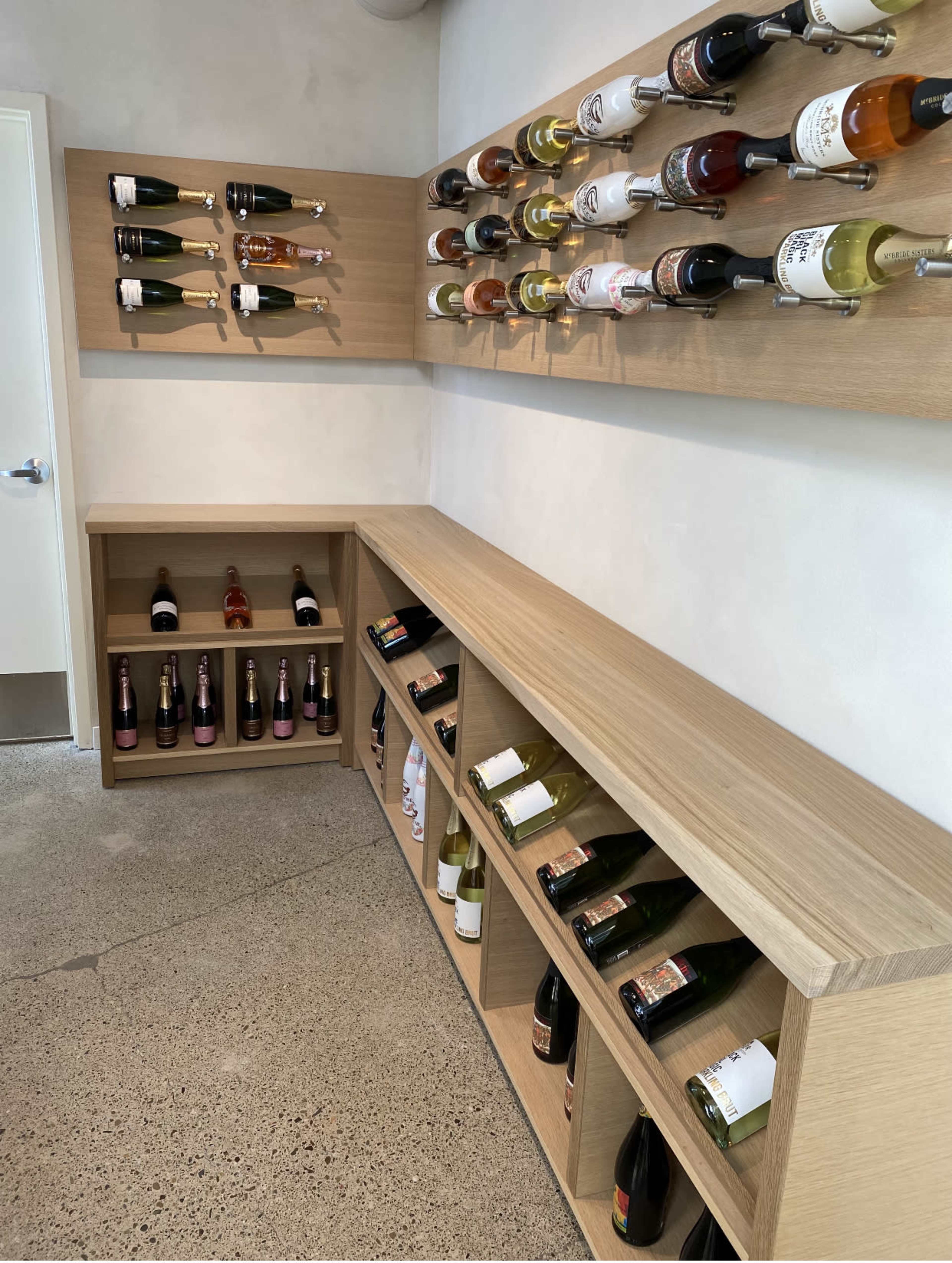 A minimalist wine display with bottles arranged neatly on wooden shelves and in storage units against a light-colored wall.