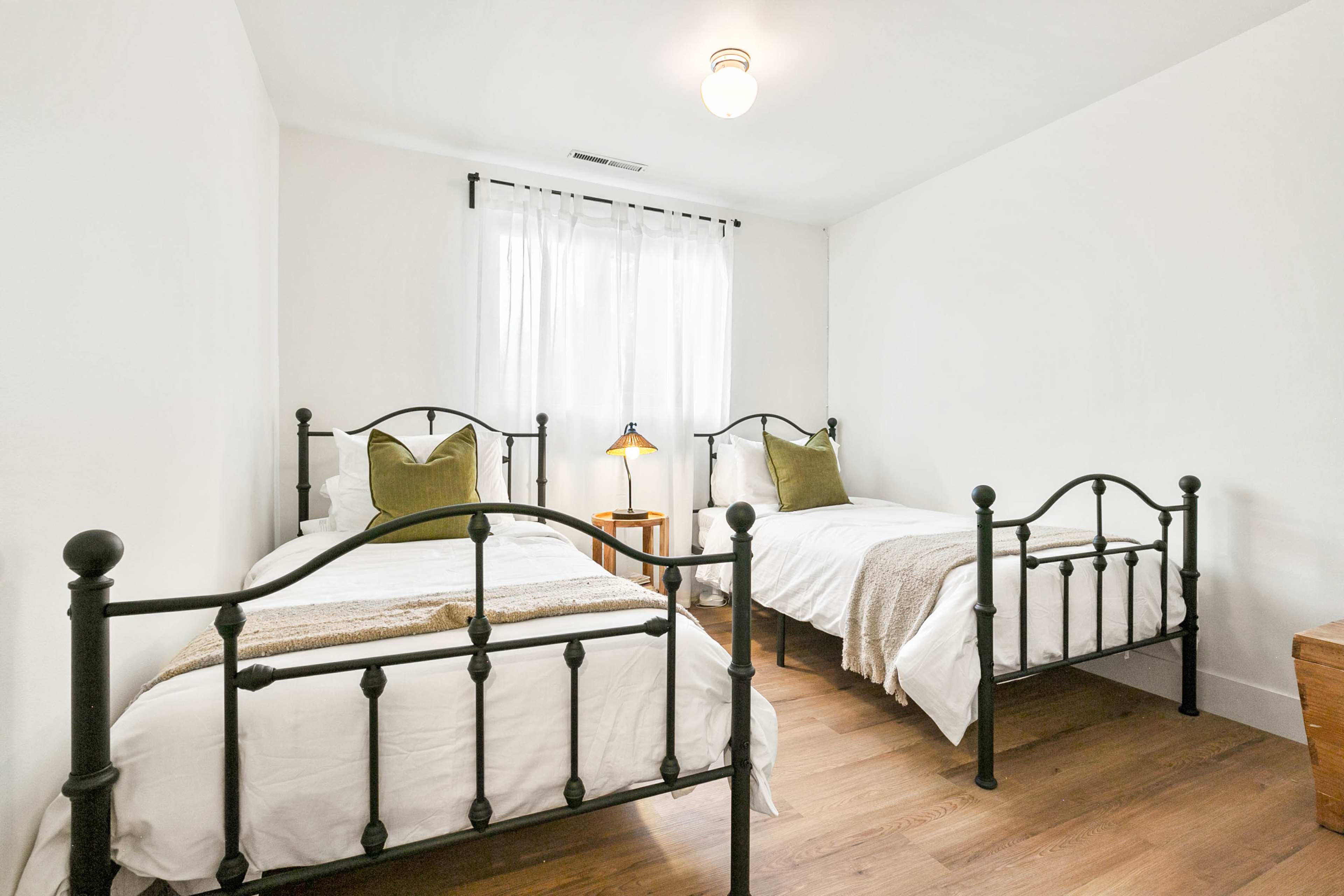 A shared bedroom features two metal-framed twin beds with white bedding, a wooden nightstand, and a window allowing natural light.