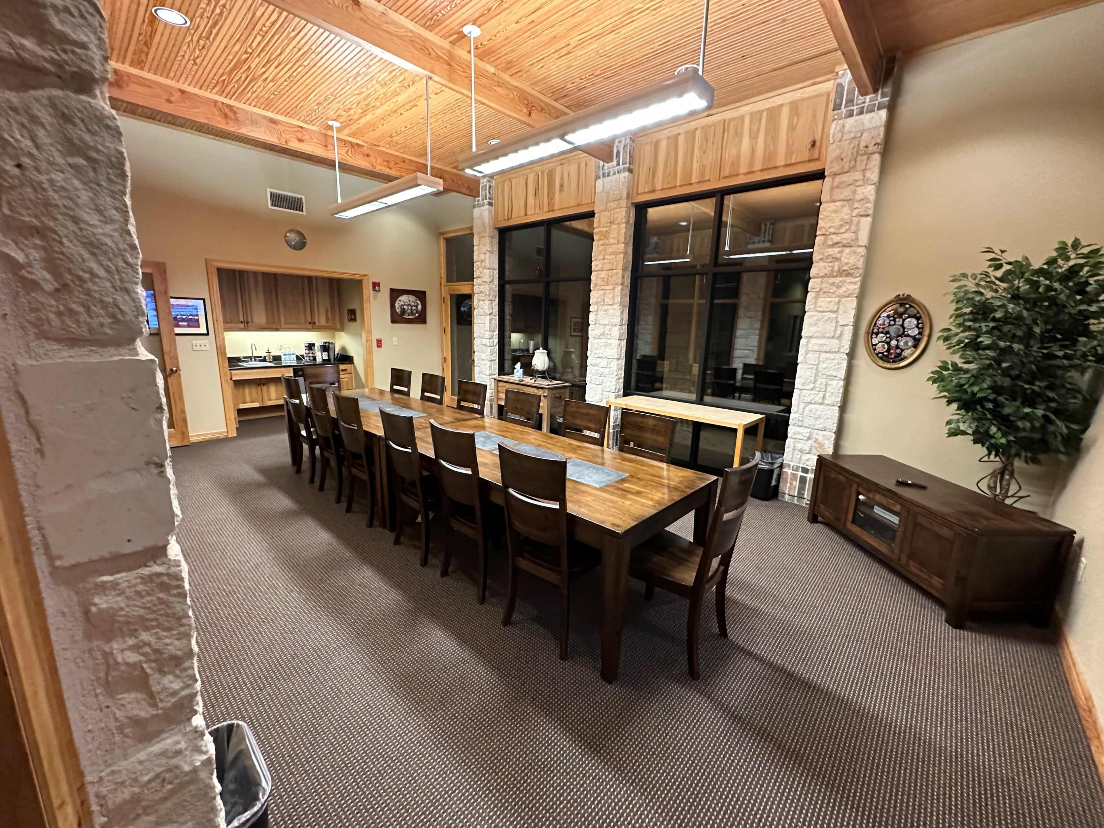 A large, wood-framed conference room with a long wooden table and multiple chairs, surrounded by windows and stone accents.