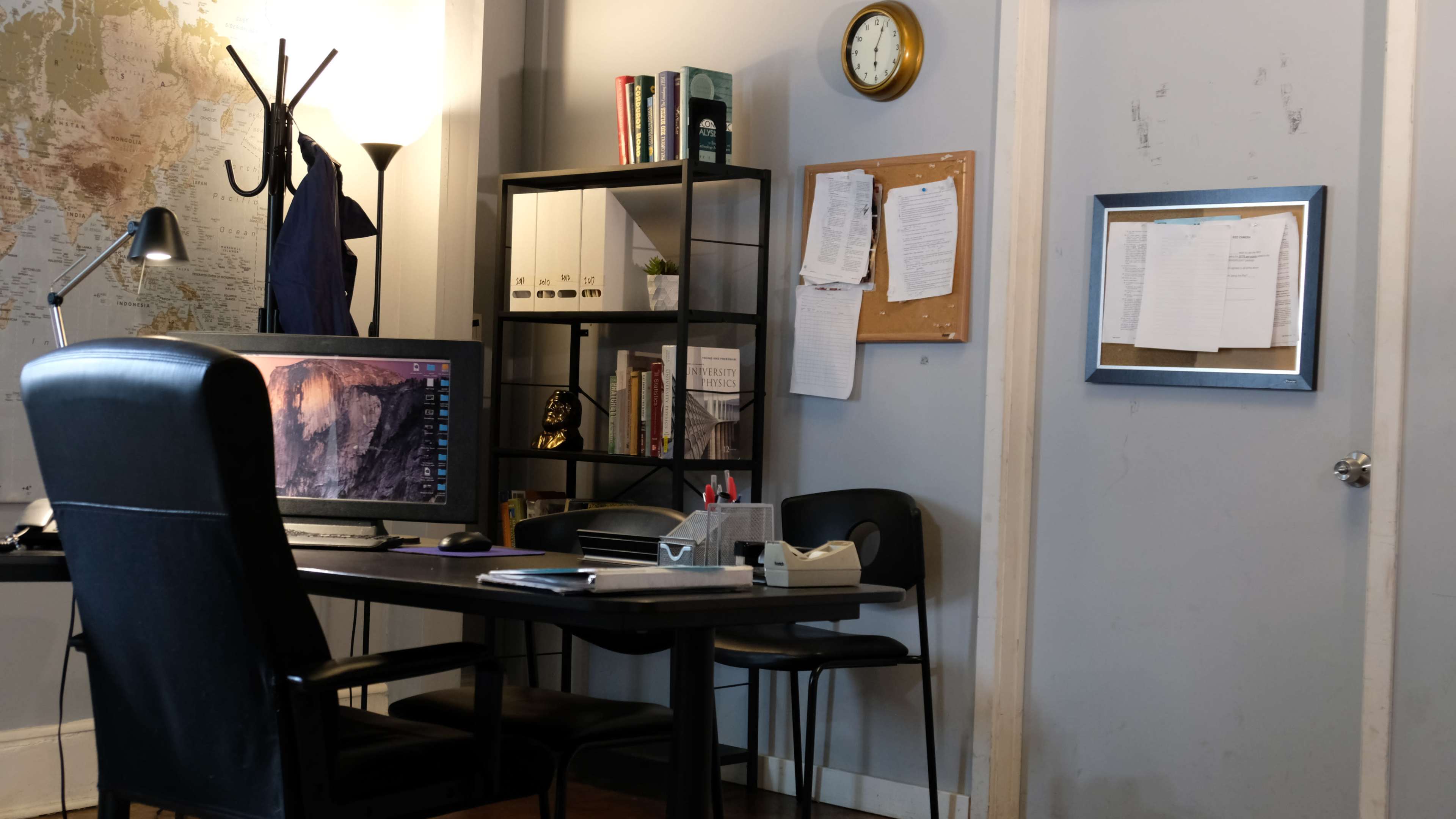 A workspace is shown with a desk, computer, shelves filled with books and files, and a bulletin board on the wall.