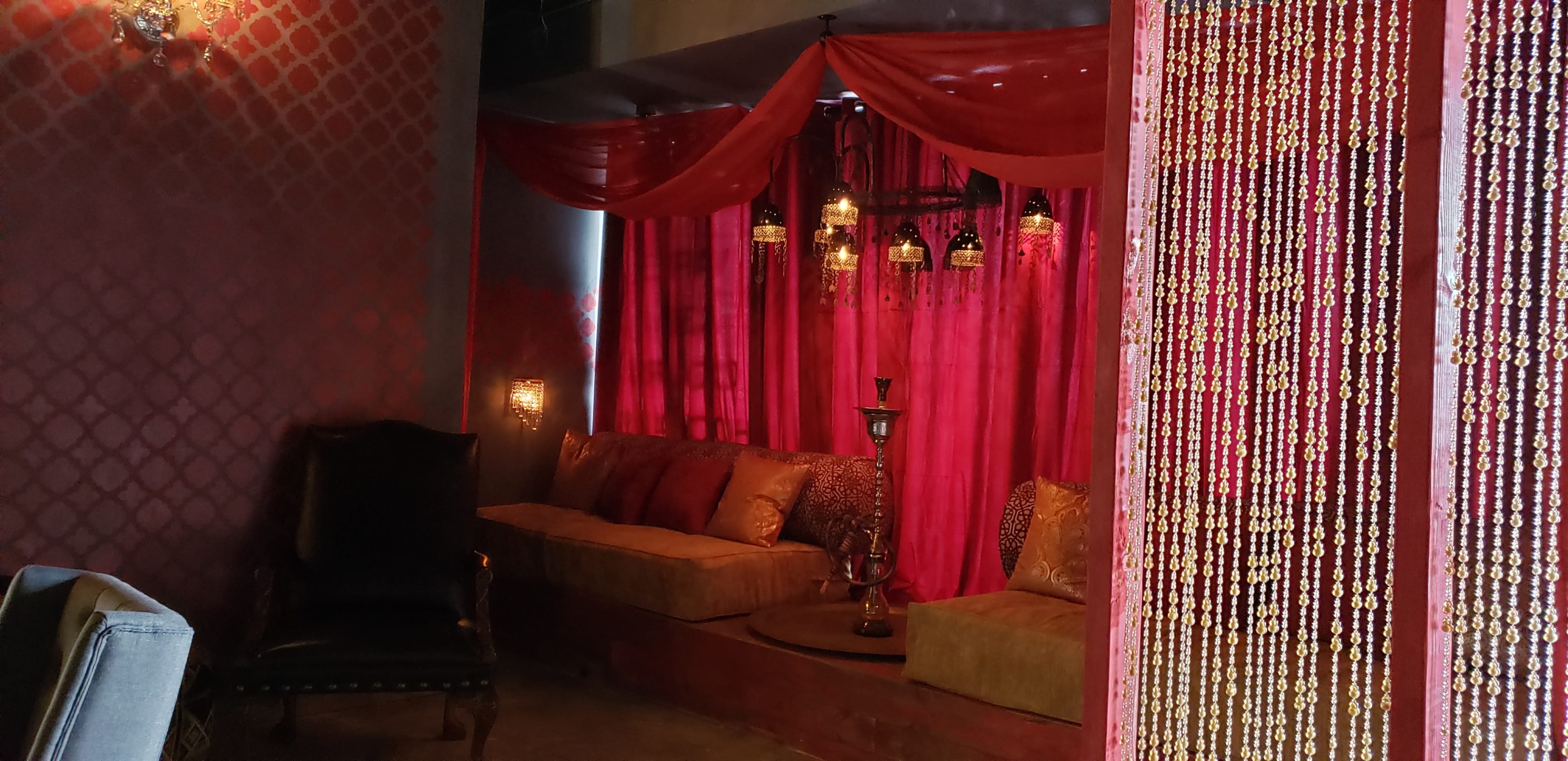 The image shows a cozy seating area adorned with red drapes and decorative lanterns, adjacent to a beaded curtain.
