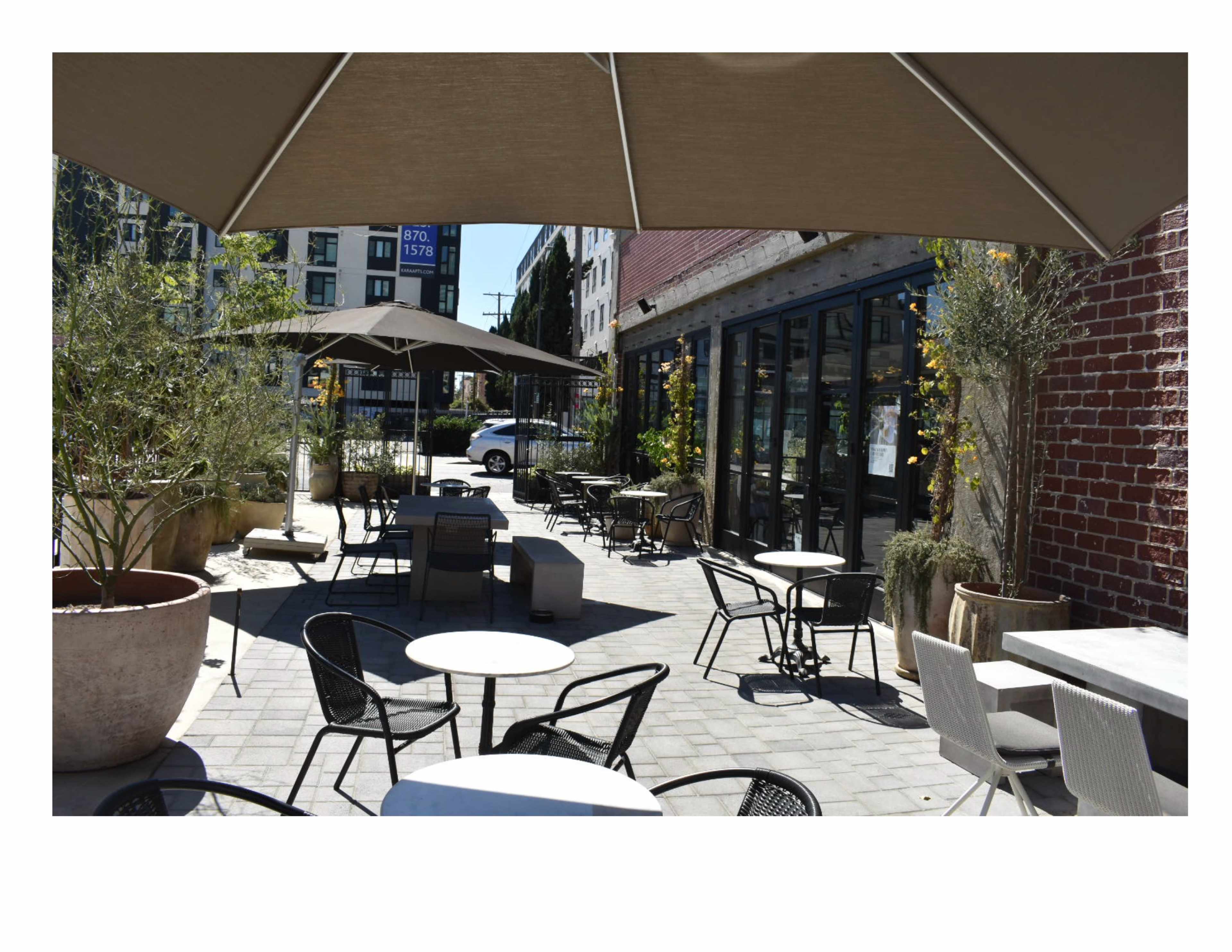 A patio area is set up with metal and wooden furniture, shaded by large umbrellas, and surrounded by planters and a brick wall.