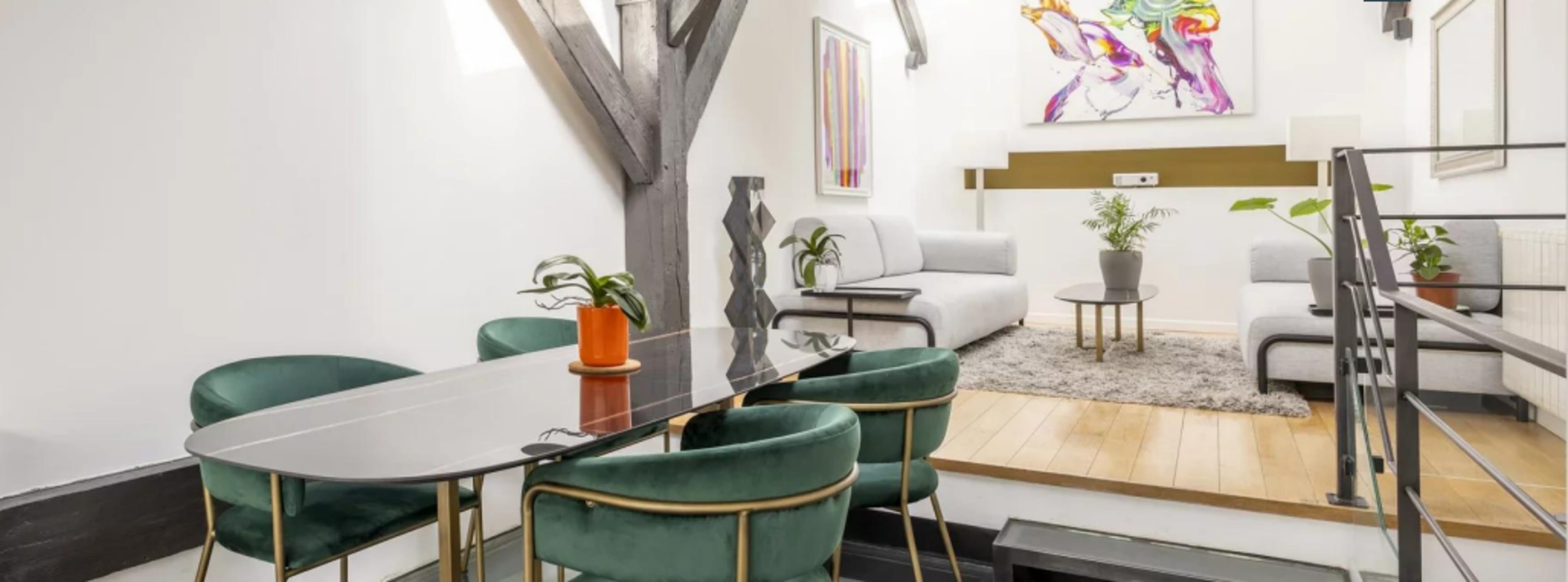 A modern living space features a dining table with green chairs, a cozy seating area with gray sofas, and decorative plants.