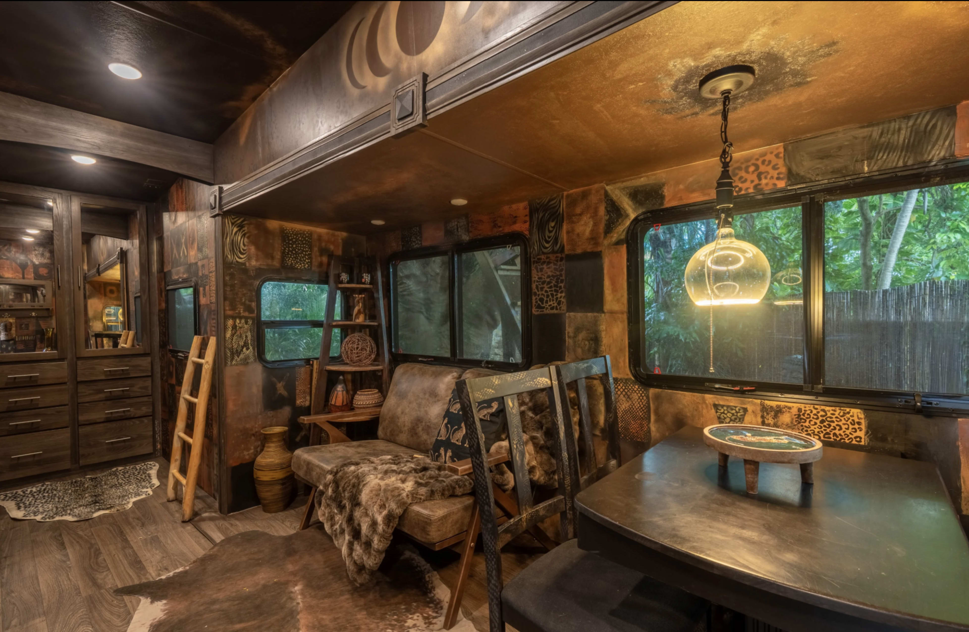 The interior of a cozy, rustic living space features a seating area with a wooden sofa, a small dining table, and walls adorned with various textured designs and earthy tones.