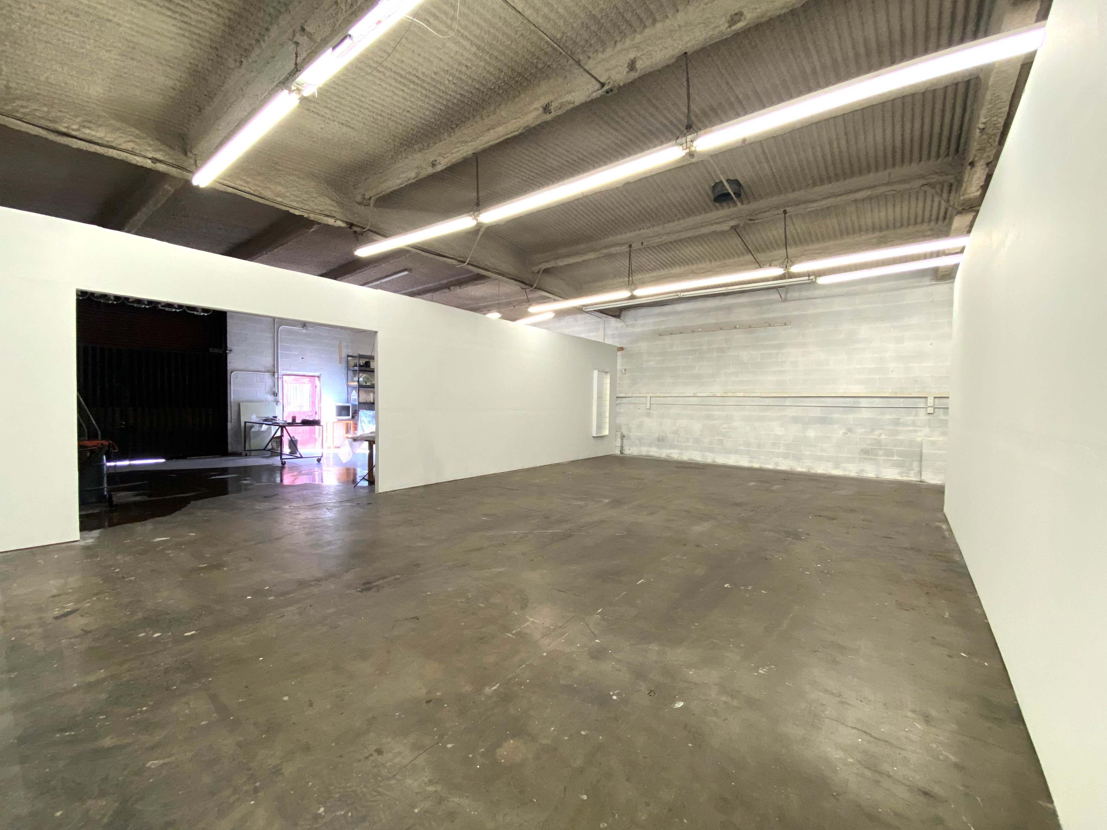 A spacious interior of a warehouse with white walls and a polished concrete floor, illuminated by overhead fluorescent lights.