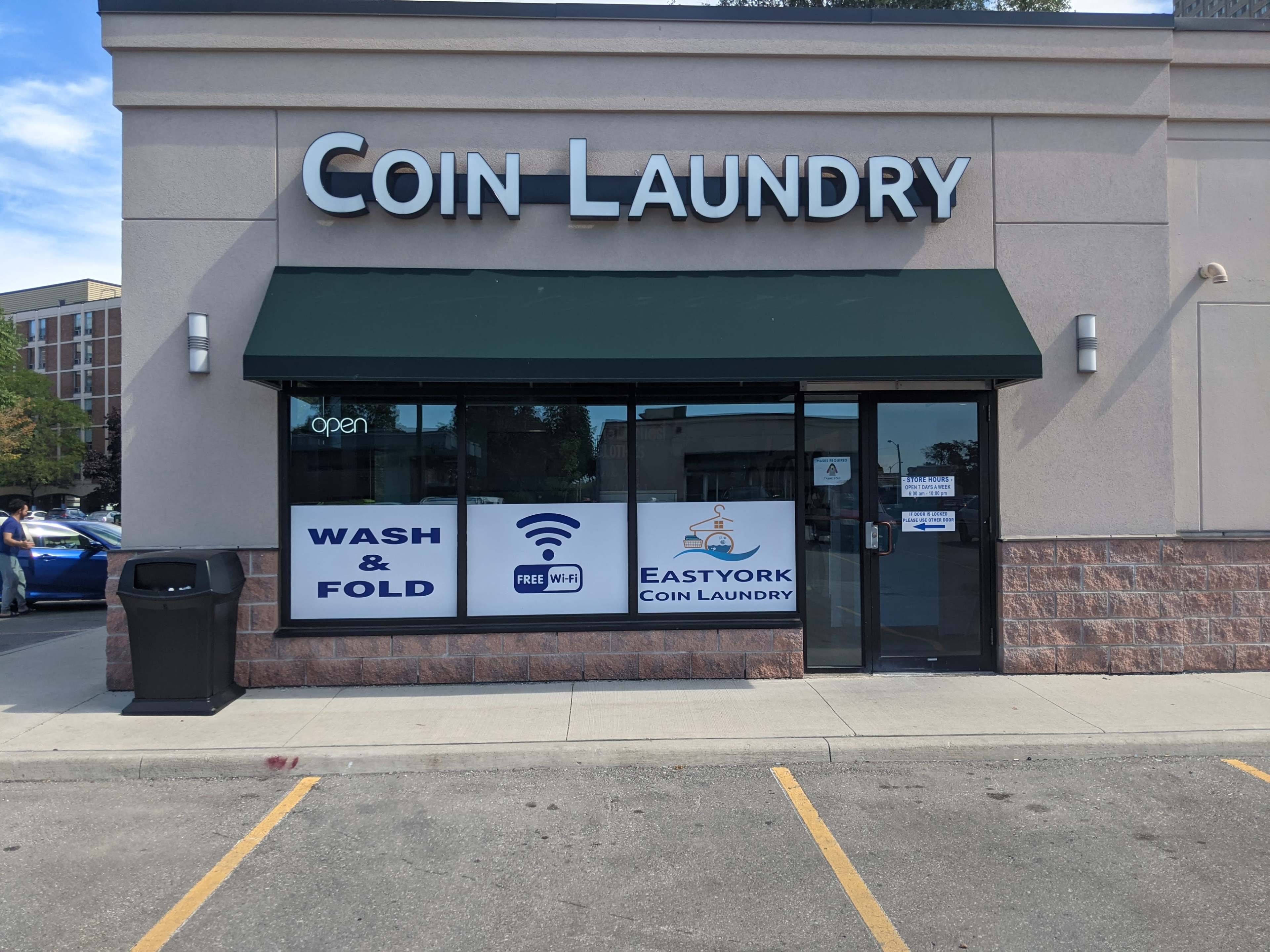 The exterior of a coin laundry facility with a green awning, featuring signs for wash and fold services and free Wi-Fi.
