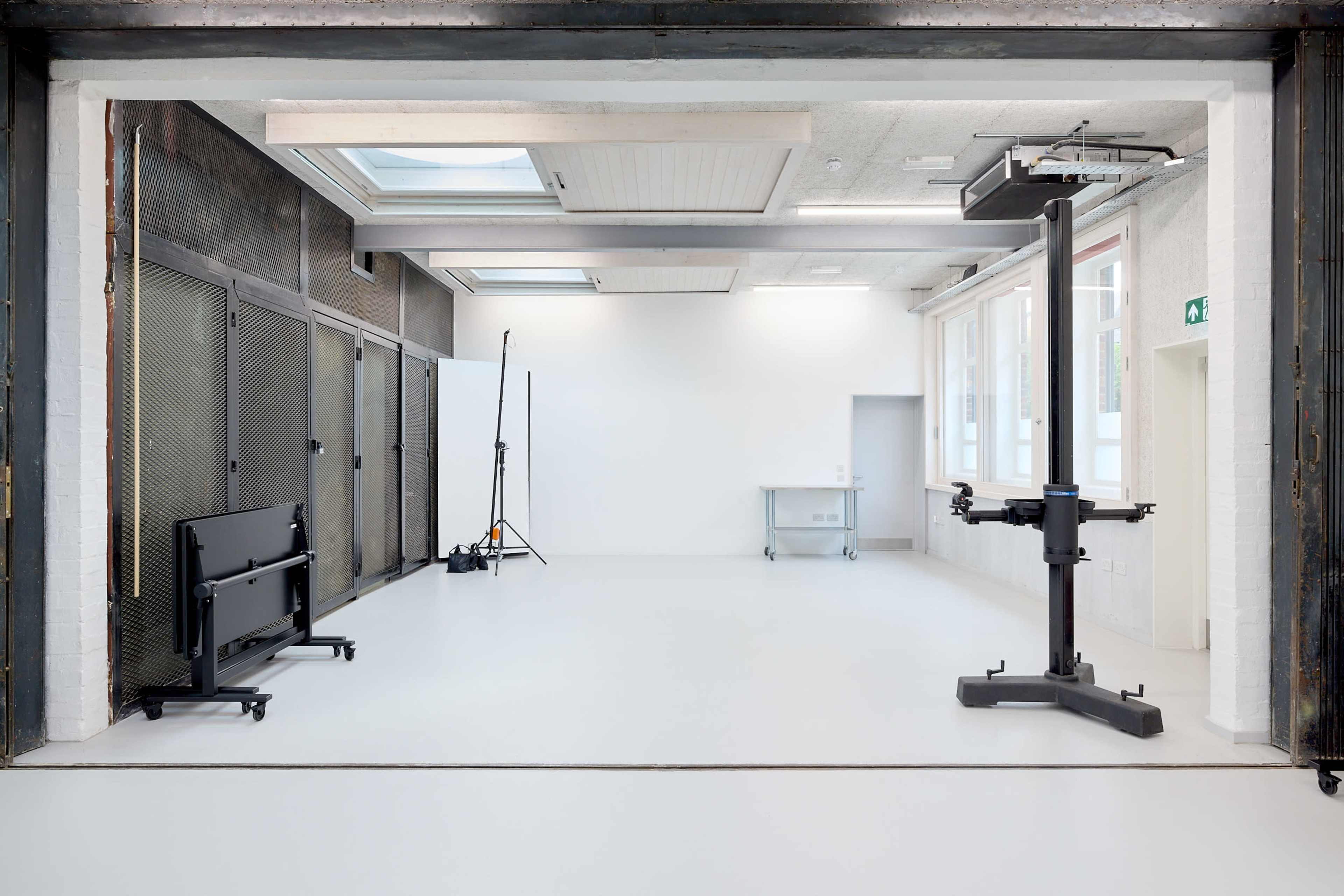 The image shows a large, empty industrial space with white walls, a smooth floor, and minimal equipment such as a lift and a table in the foreground.