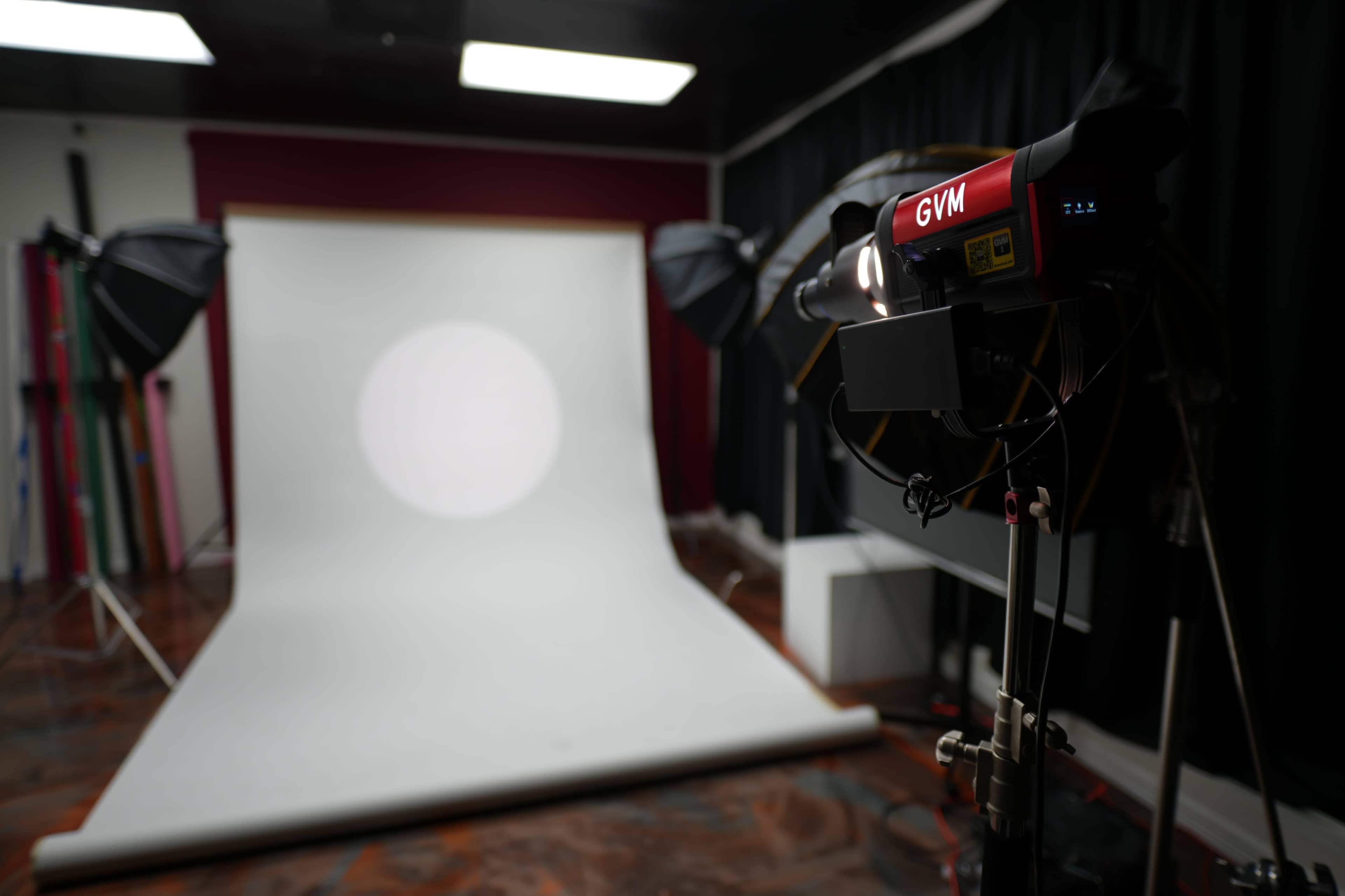 The image shows a photography studio with a backdrop and multiple lights set up for shooting.