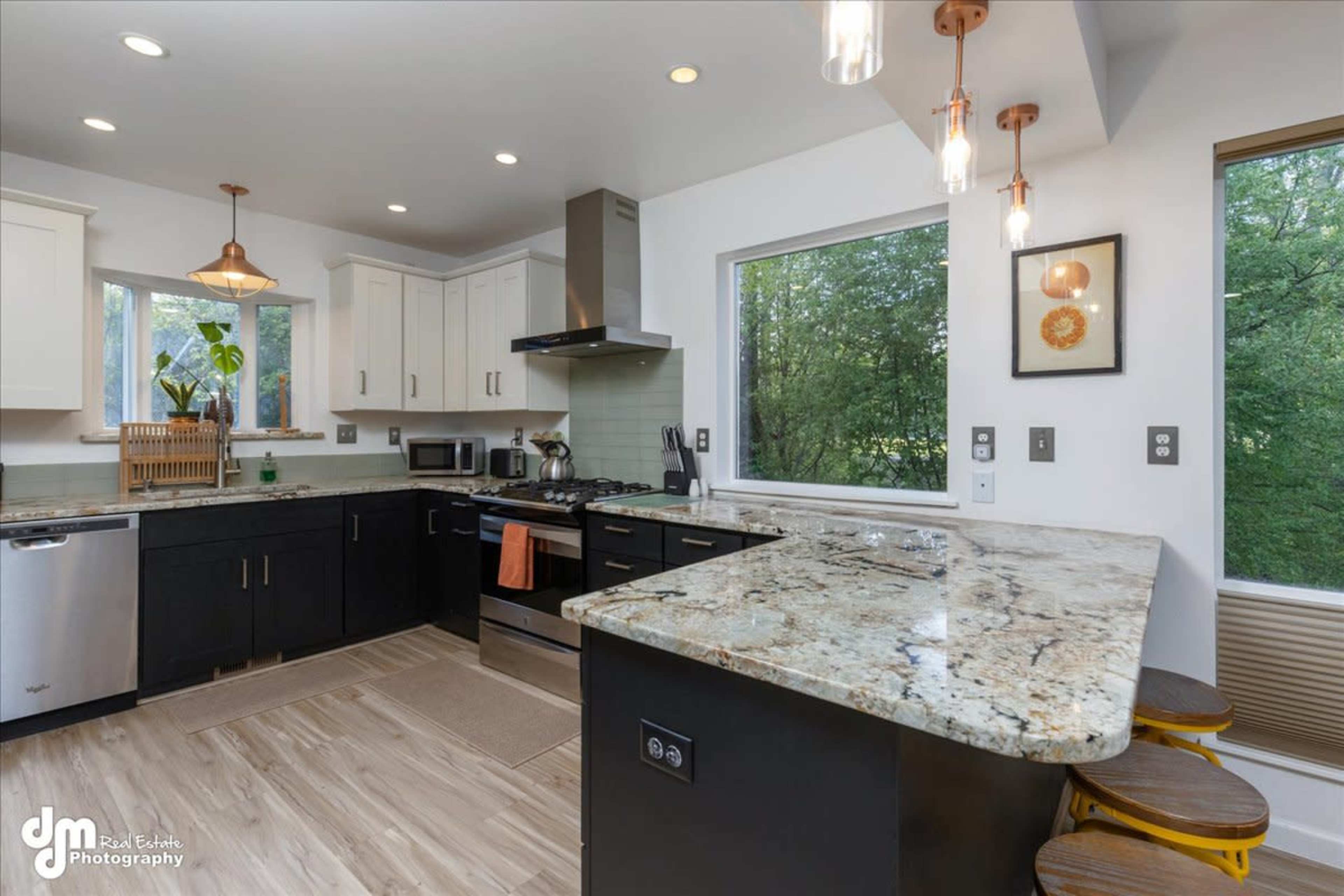 A modern kitchen features white and black cabinetry, a granite countertop, stainless steel appliances, and large windows overlooking greenery.
