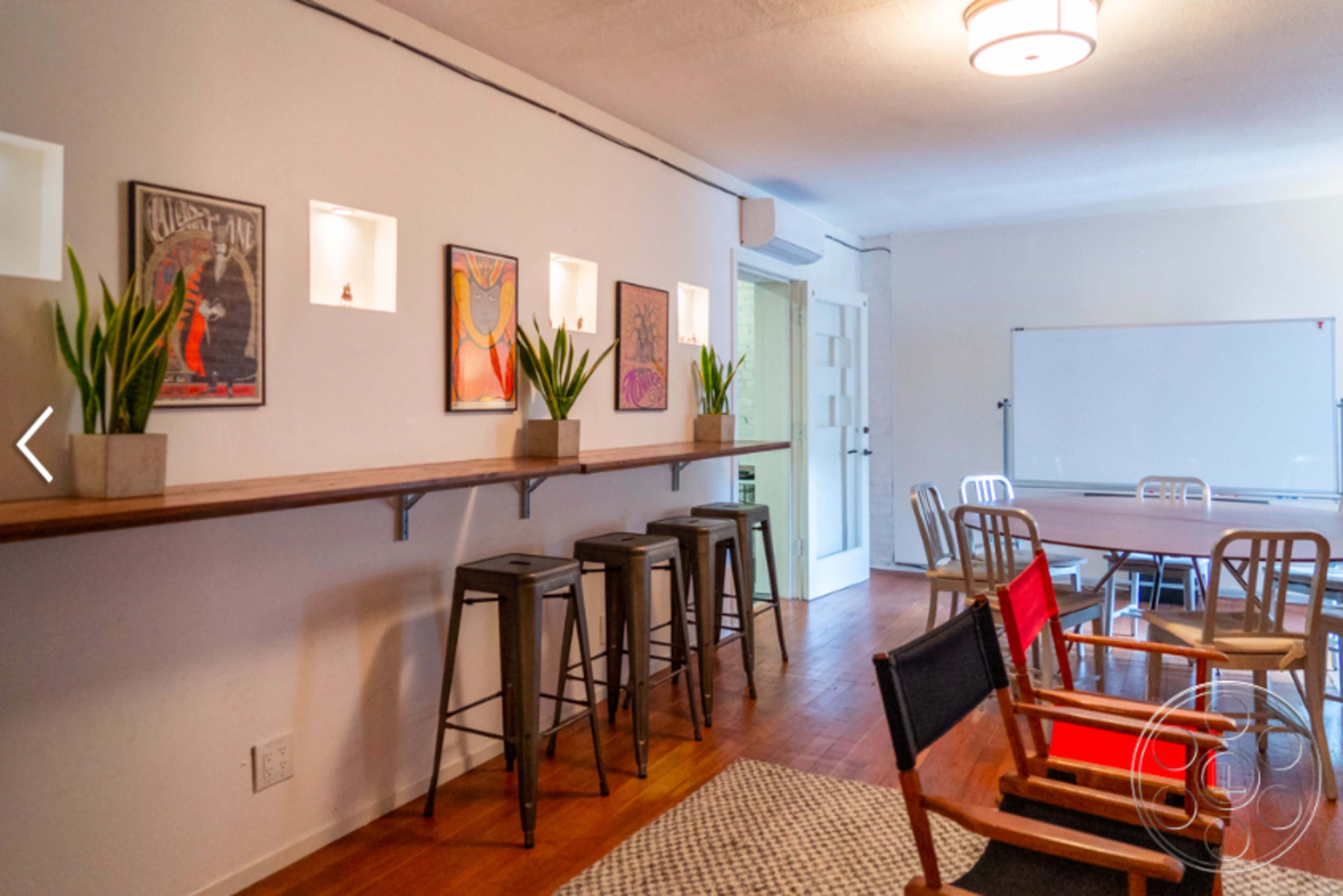 The image shows a modern meeting room with a long wooden table, several chairs, and decorative wall shelves featuring potted plants and framed artwork.