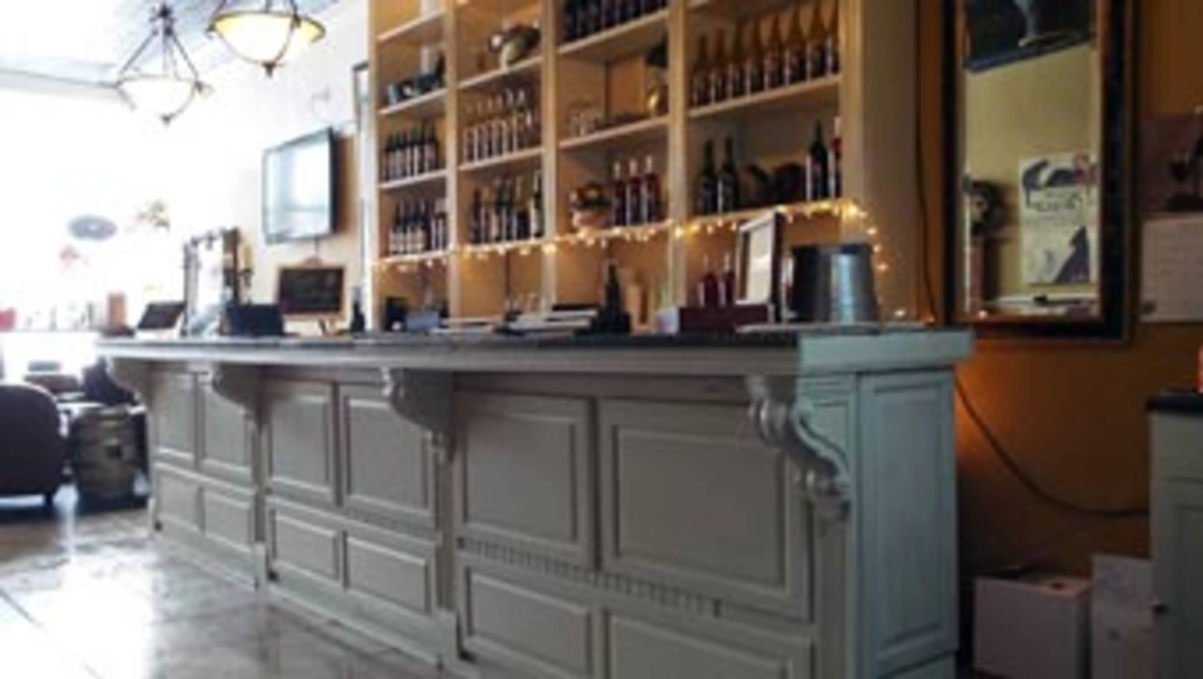 A wooden bar with a neatly organized shelf of bottles and a mirror on the wall behind it.