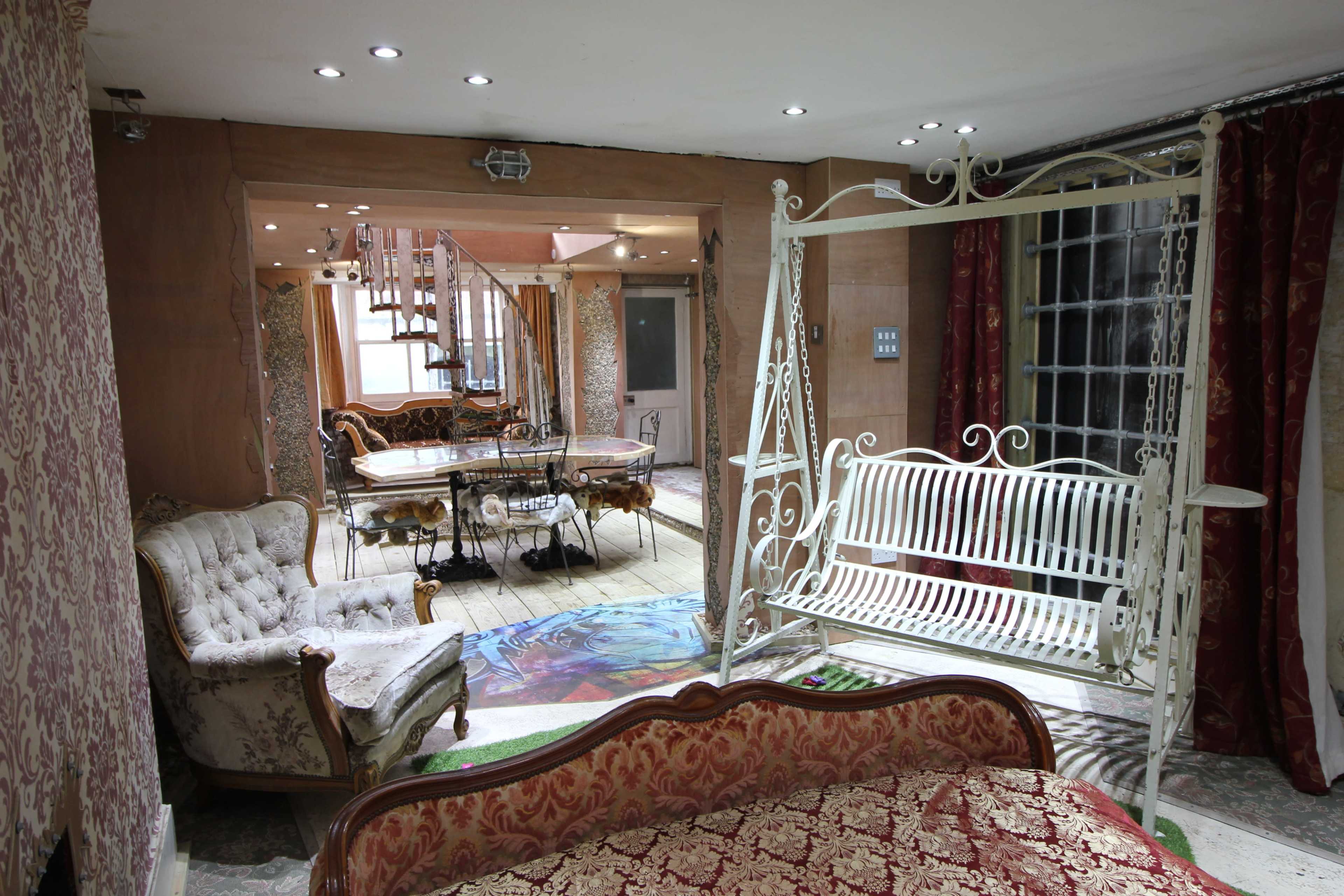 A room divided into a cozy seating area with vintage furniture and a dining space featuring a glass table and decorative elements.