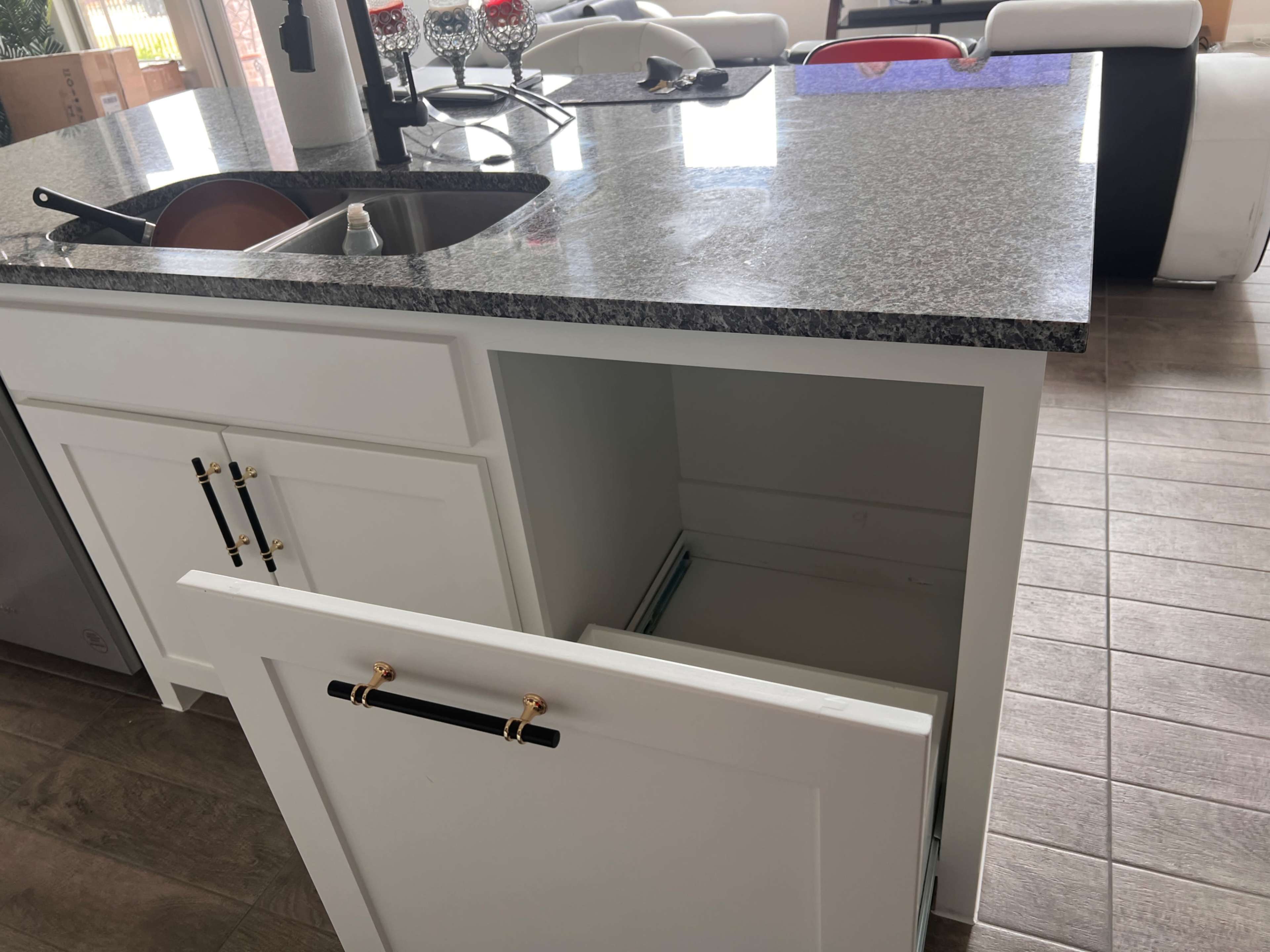 A modern kitchen features a granite countertop with a sink and an open cabinet underneath.