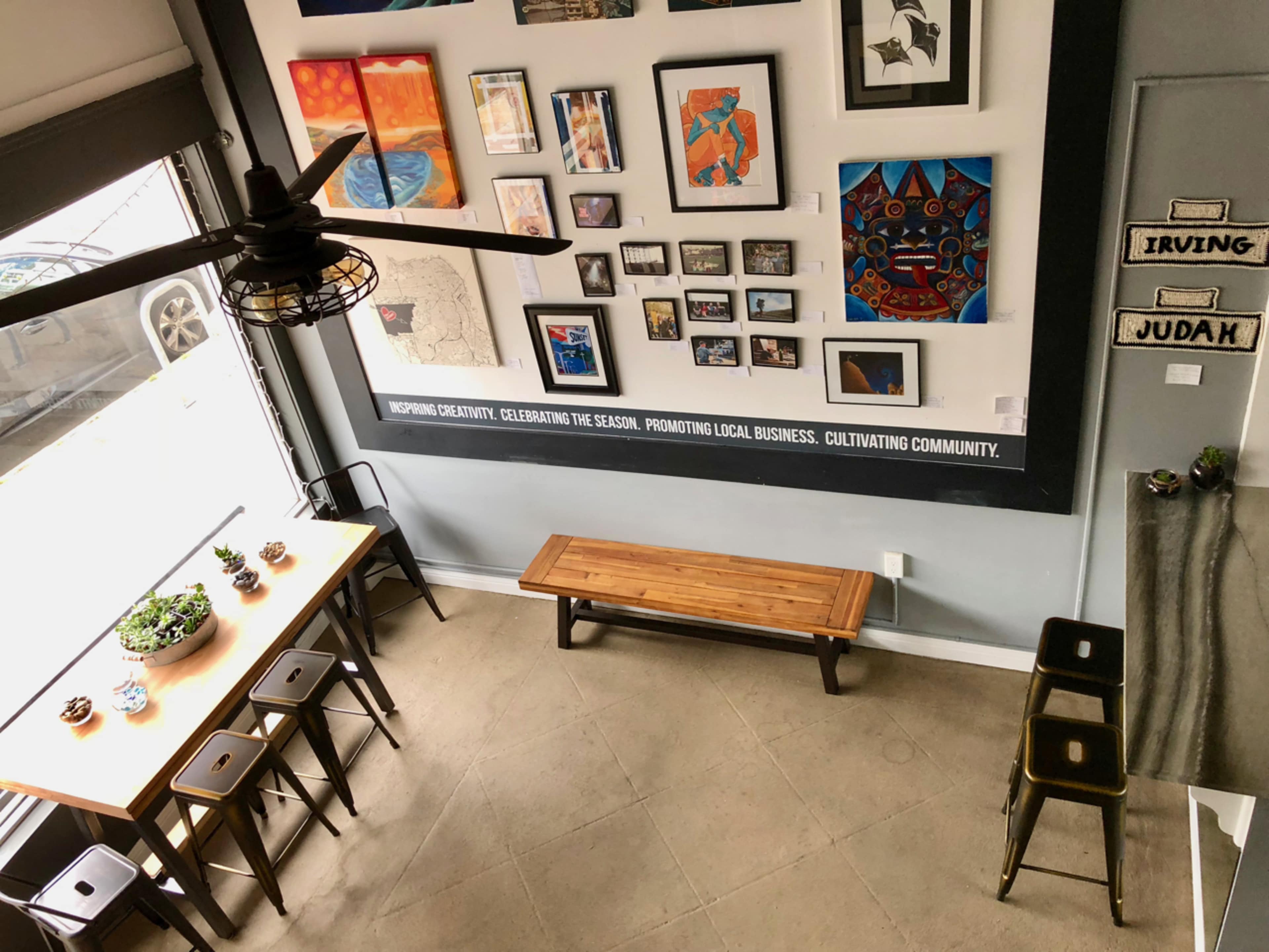 A modern indoor café with a wooden dining table, benches, and a wall adorned with various artworks.