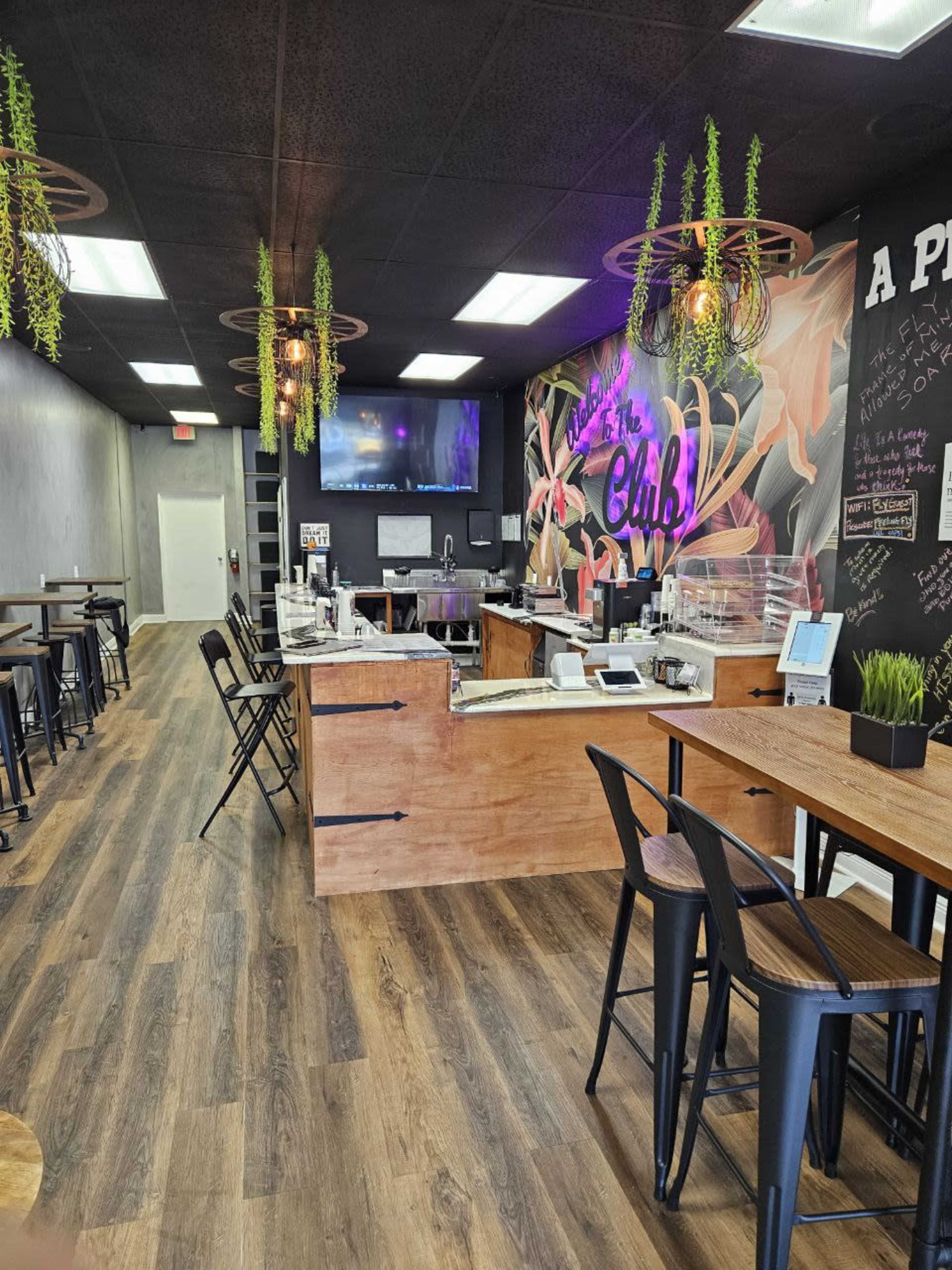 The interior of a modern cafe with wooden flooring, a service counter, and seating arrangements along the walls.