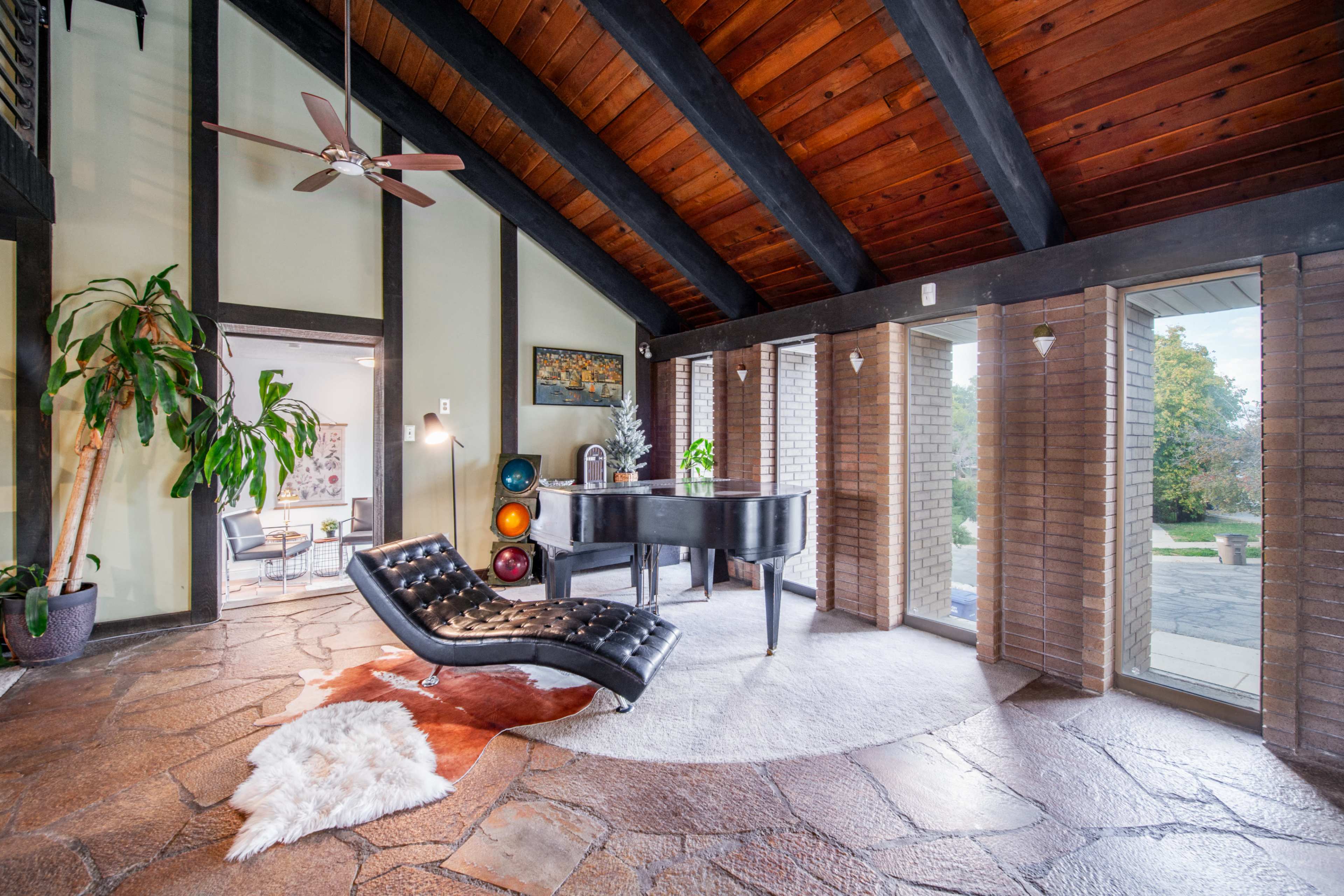 A room featuring a black piano, a modern chaise lounge, and large windows that open to a patio with outdoor scenery.
