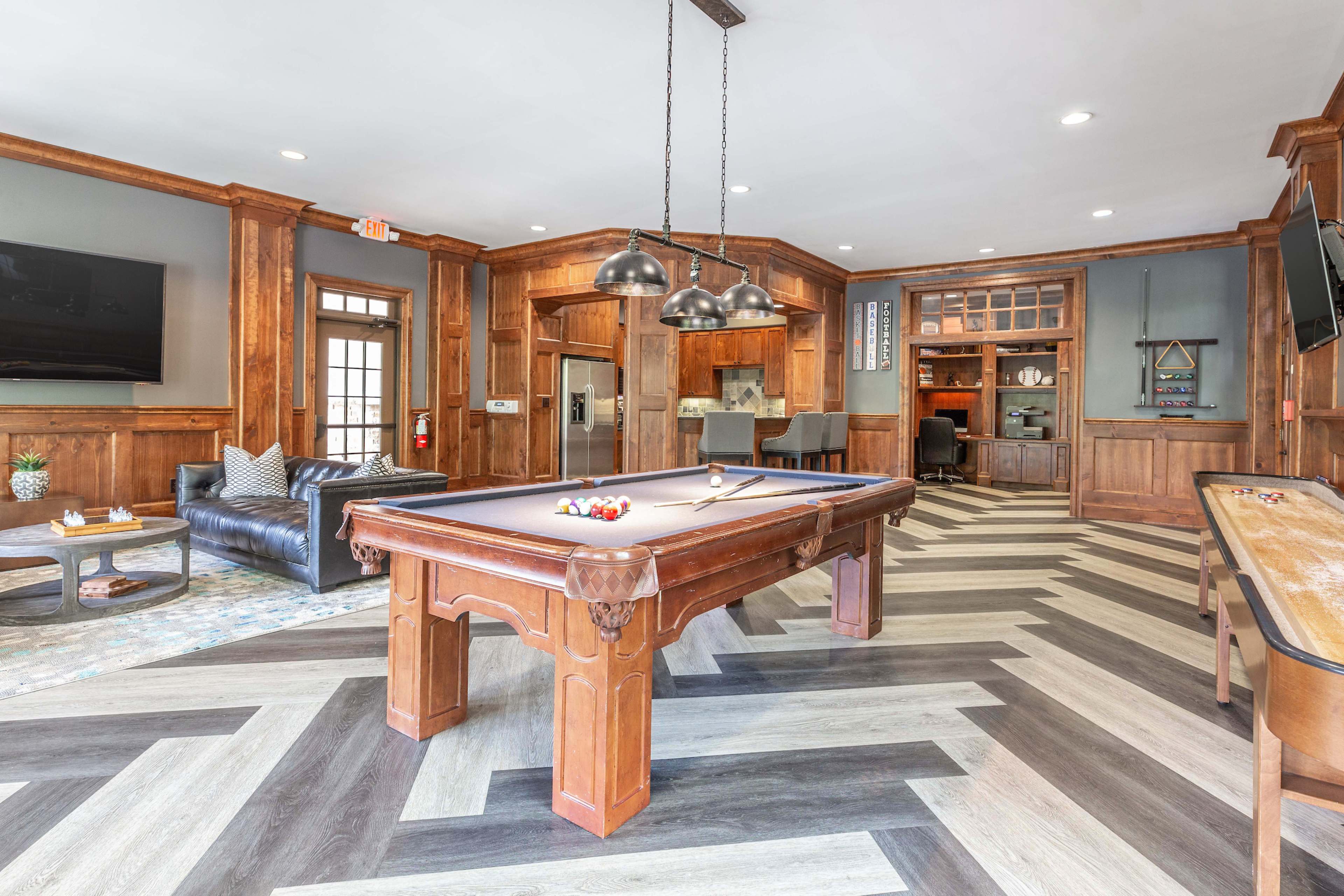 A room with a pool table, a leather sofa, and a wooden floor arranged in a herringbone pattern.