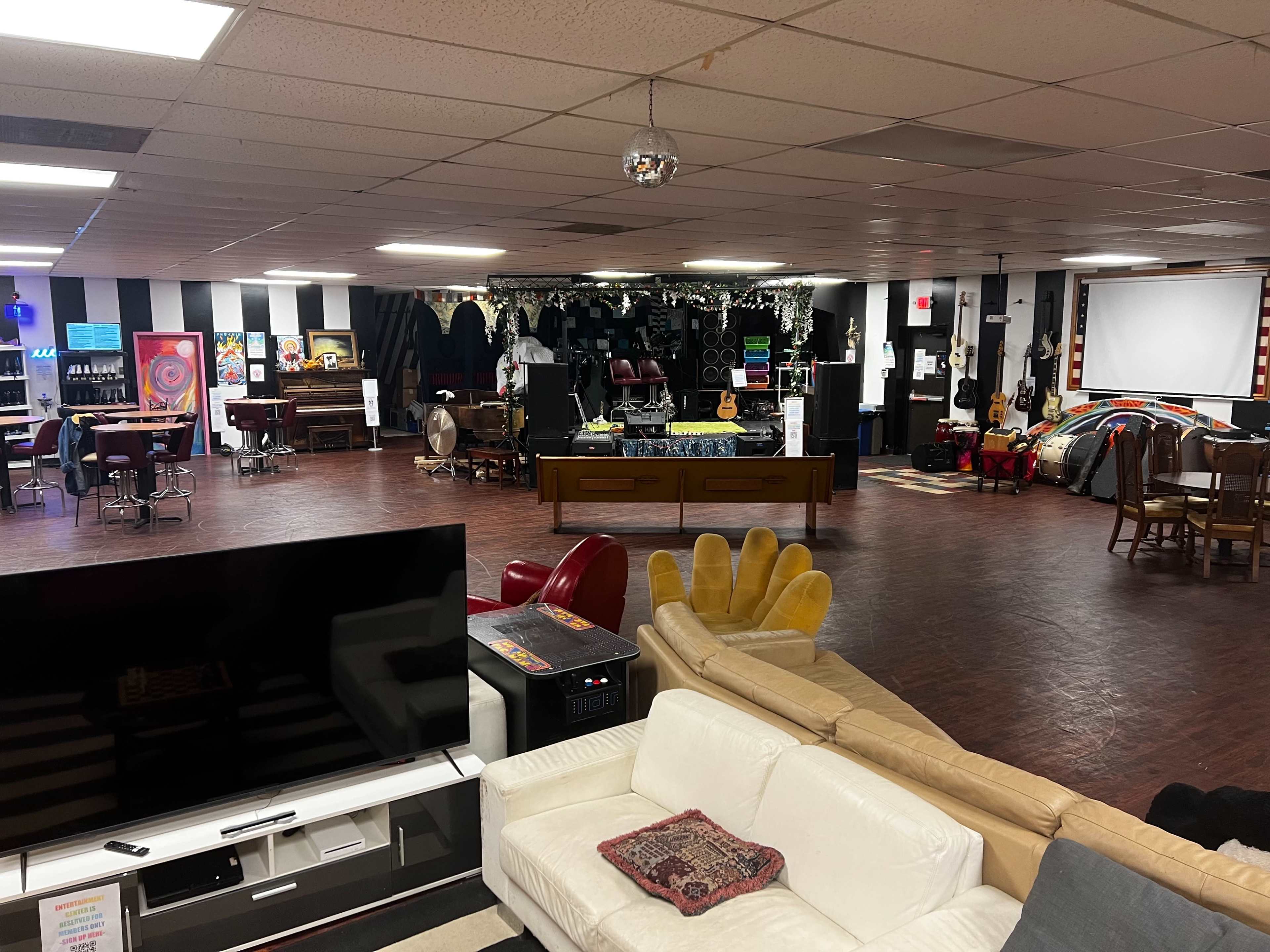 A spacious indoor venue with a stage at one end, various seating arrangements, and decorations, including musical instruments and art on the walls.