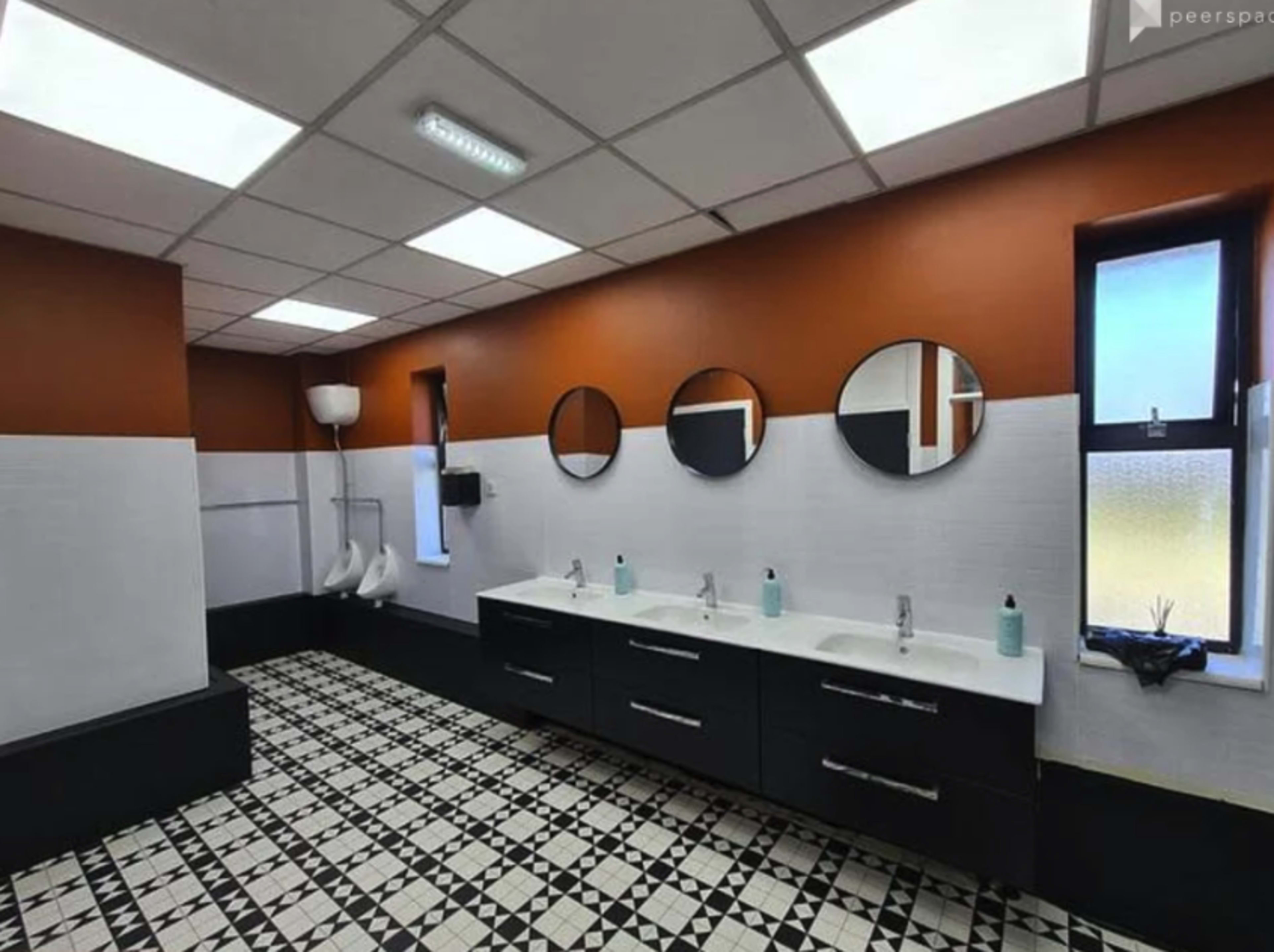 The image shows a modern bathroom with multiple sinks, mirrors, and a black and white tiled floor.