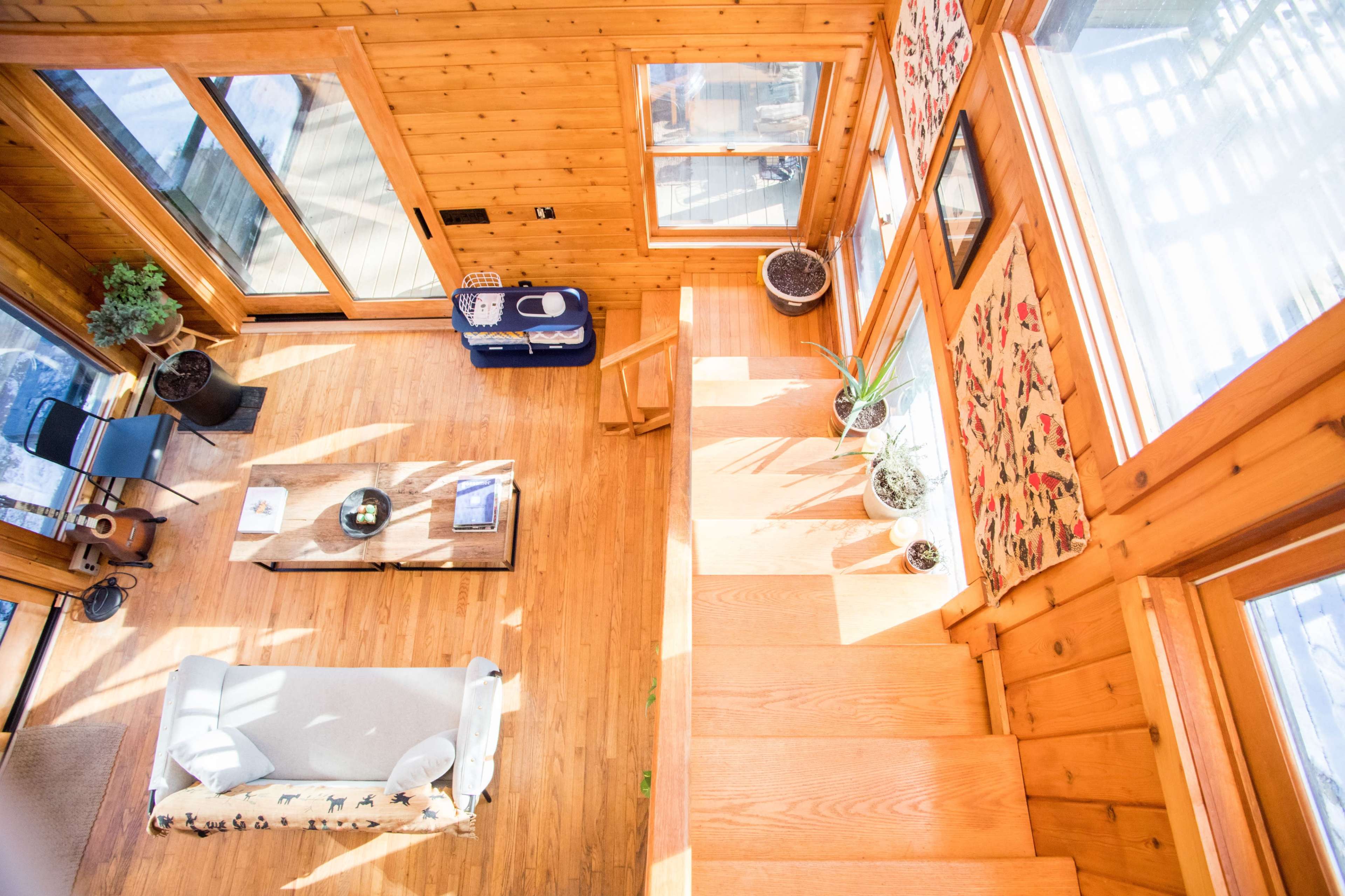 A wooden interior of a house with an open space, featuring a living area with a sofa, a coffee table, and stairs leading to an upper level.