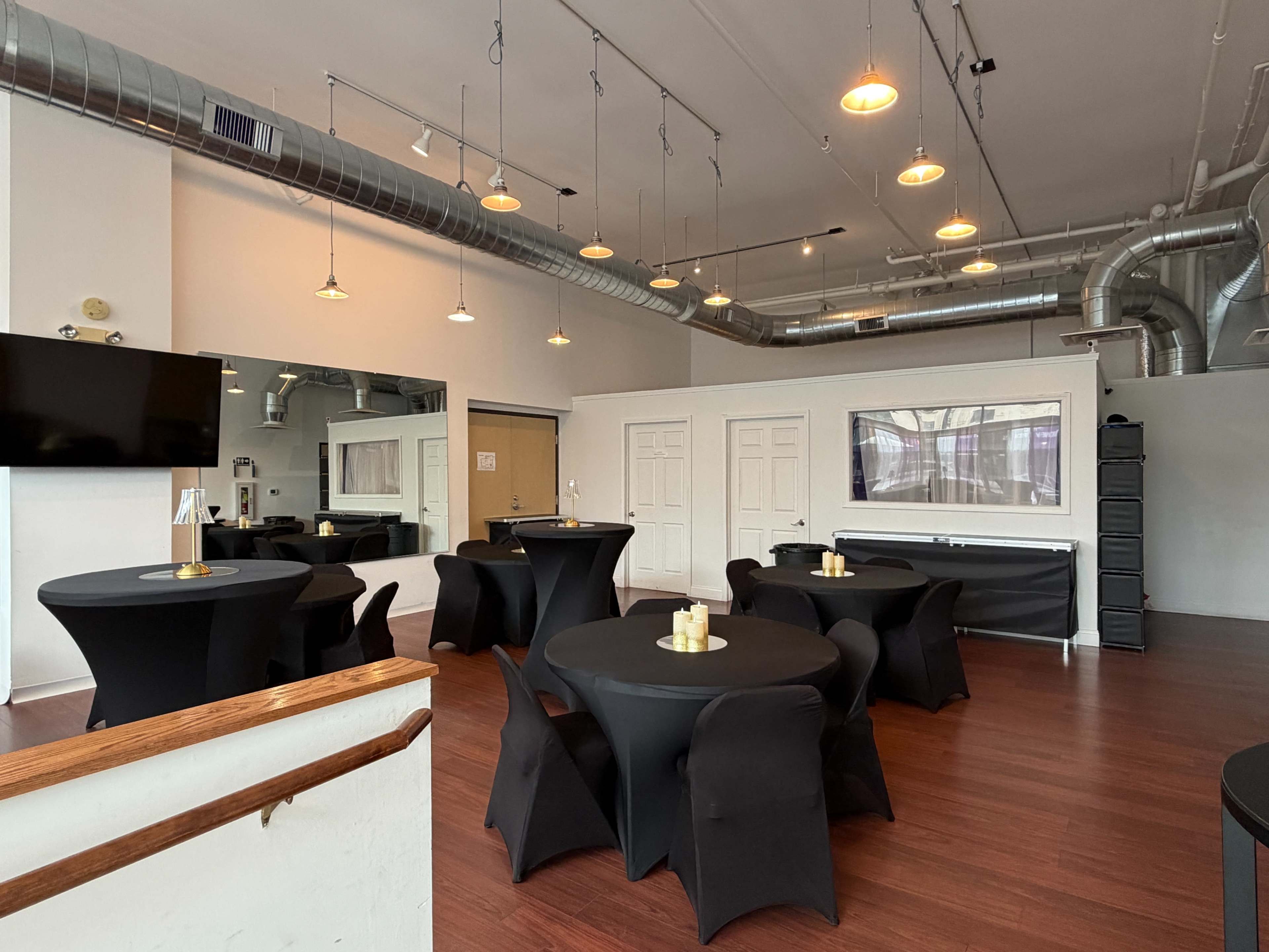 The image shows a spacious event room featuring black tables with candles, a mirrored wall, and modern lighting fixtures.